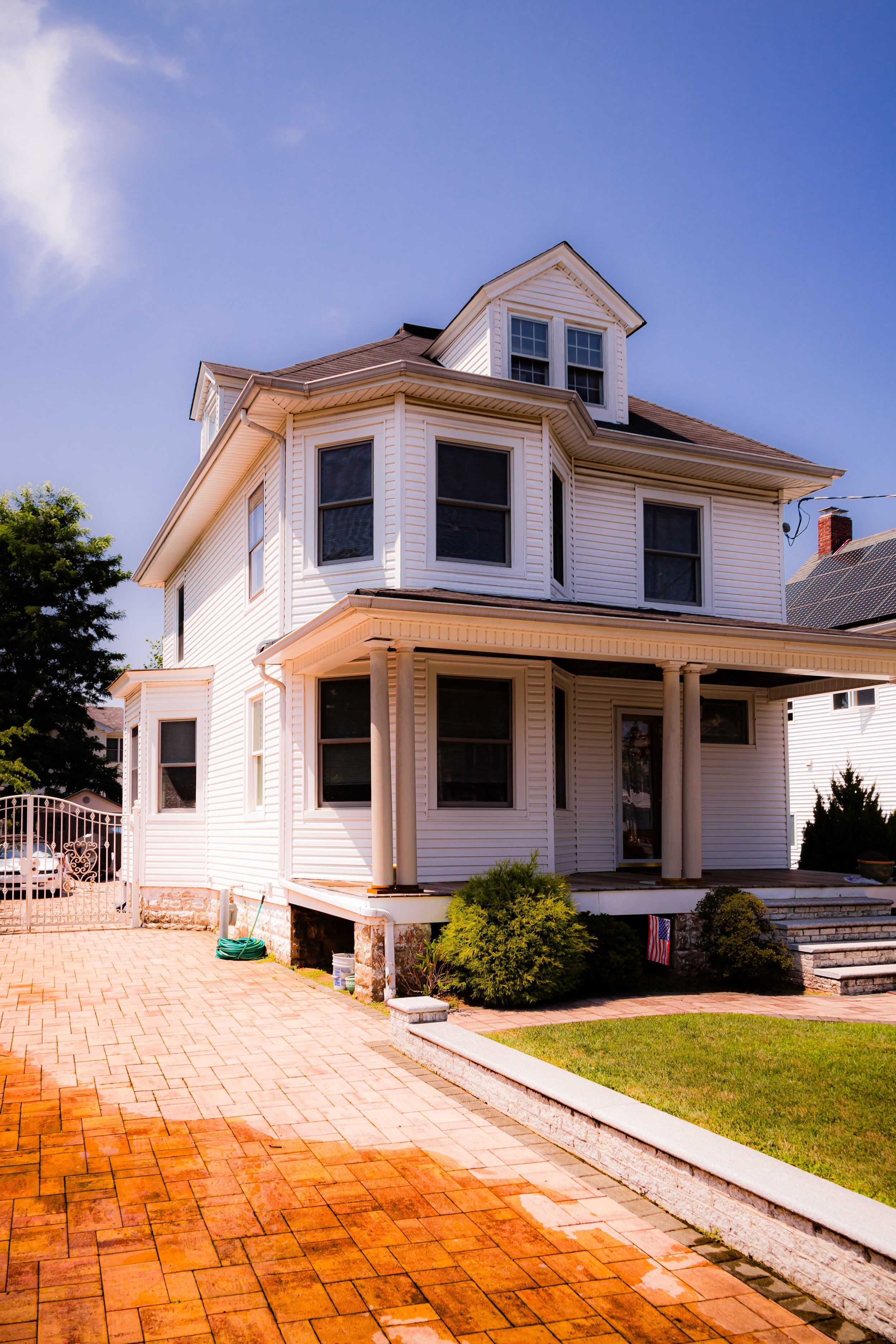 White Victorian-style house with front porch, multiple windows, and a small attic dormer under a clear blue sky.