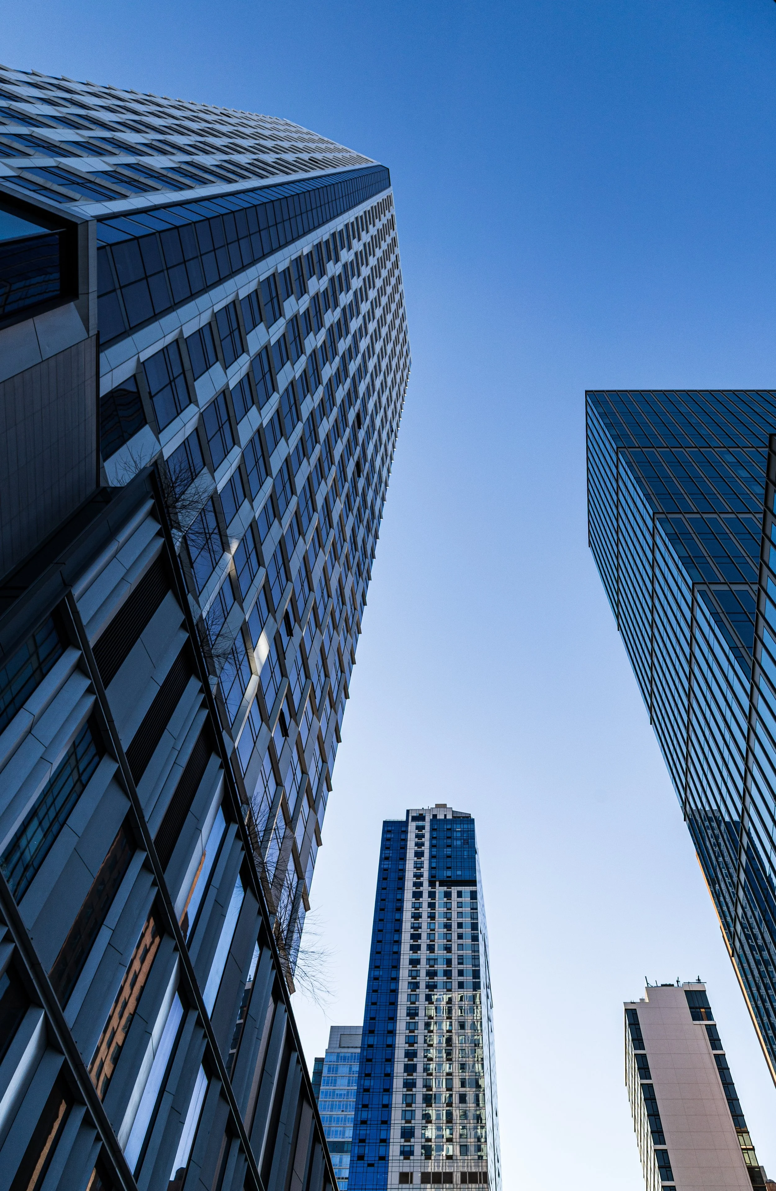 Low-angle view of tall modern skyscrapers with glass facades against a clear blue sky.