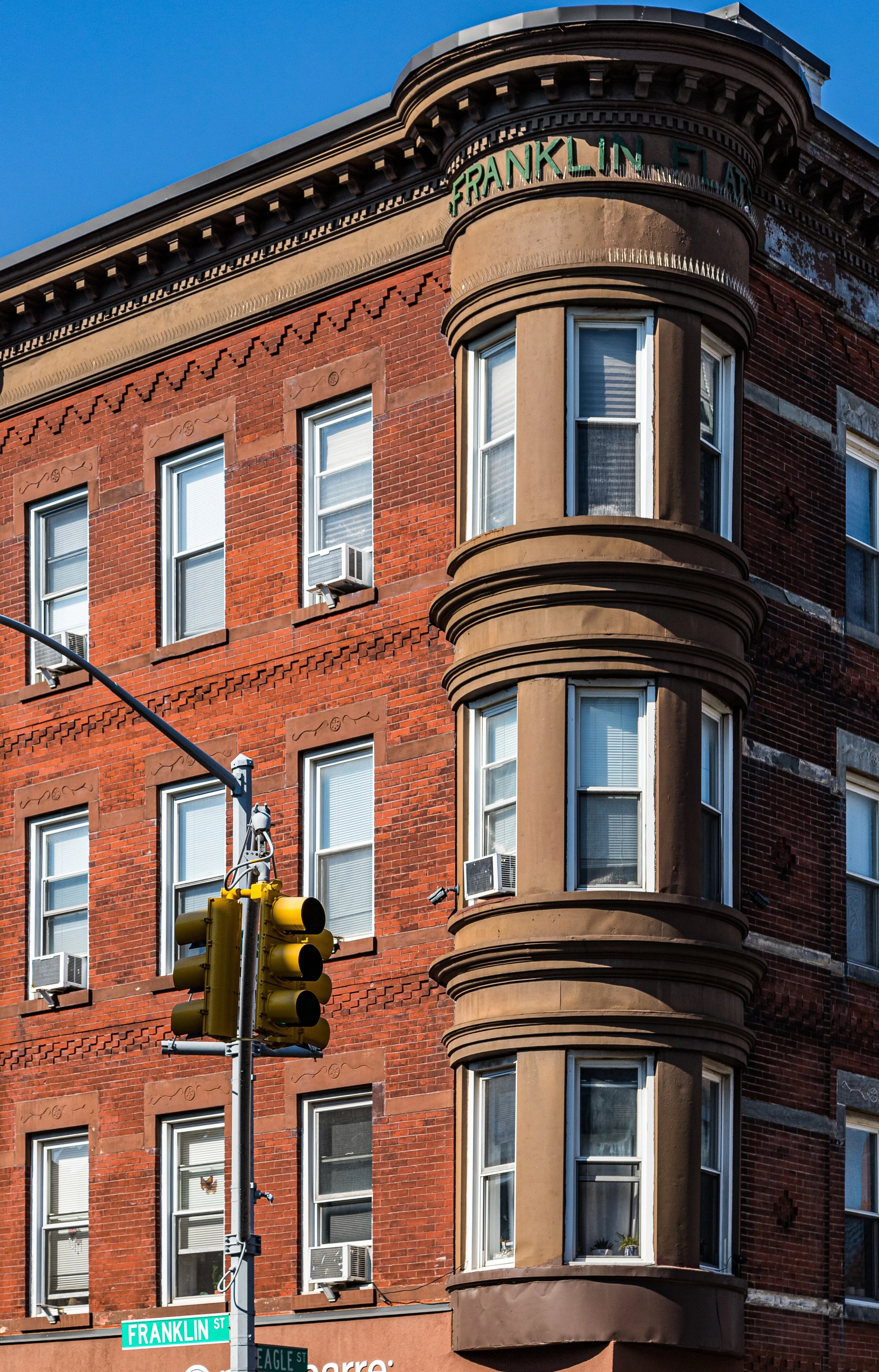 A red-brick building on Franklin Street with bay windows and air conditioning units, a traffic light, and a street sign on the corner.