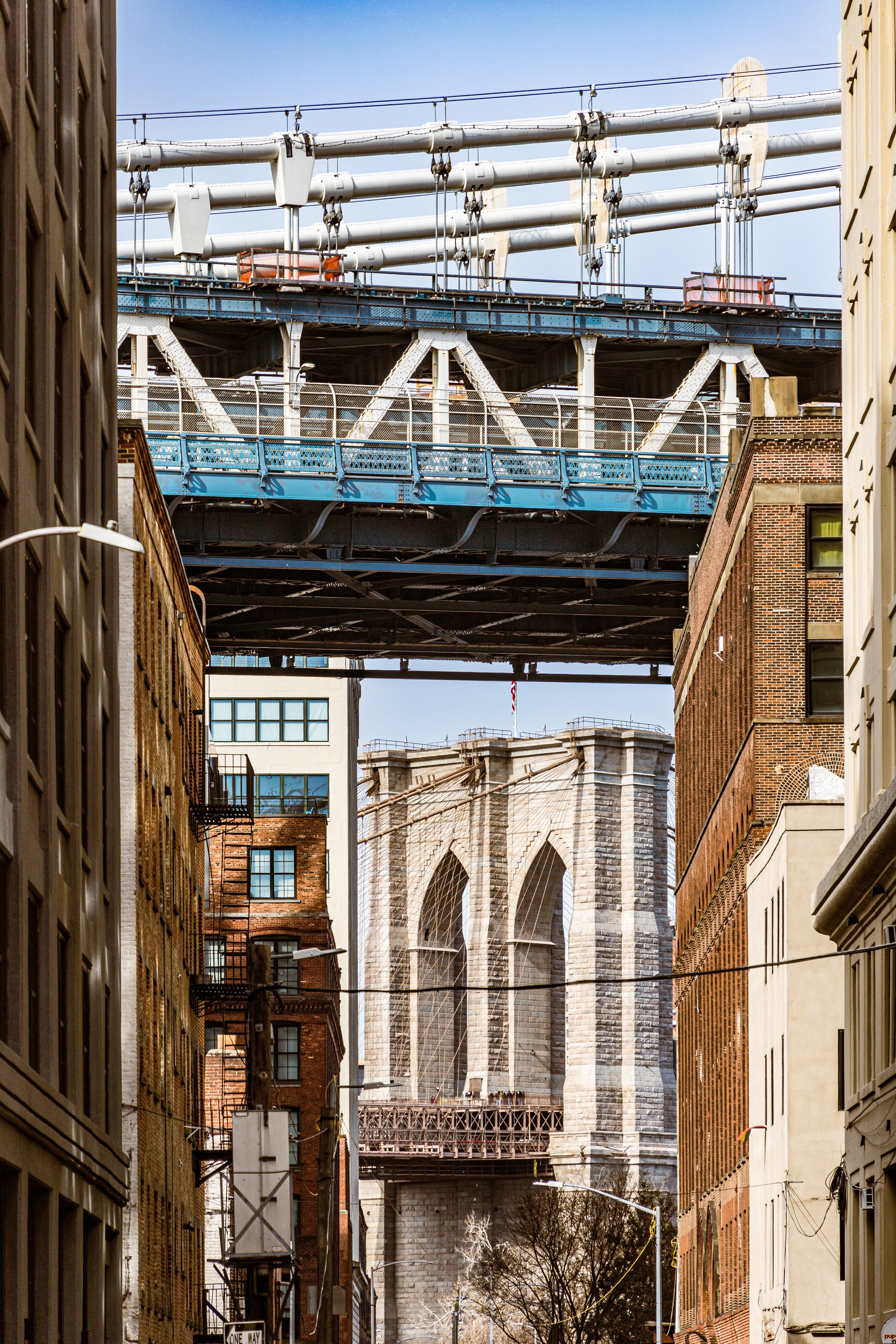 City street view with the Brooklyn Bridge in the background, viewed from a narrow alley between tall buildings.