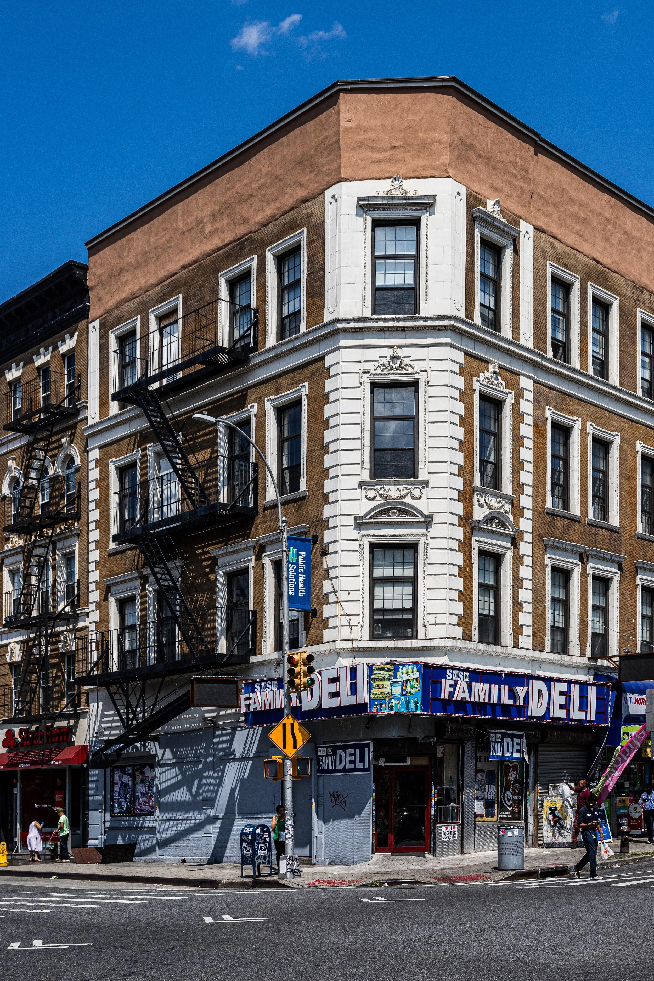 Corner building on city street with storefront signage for Family Deli, a blue SignHealth Solutions banner, and pedestrians walking by on sunny day.