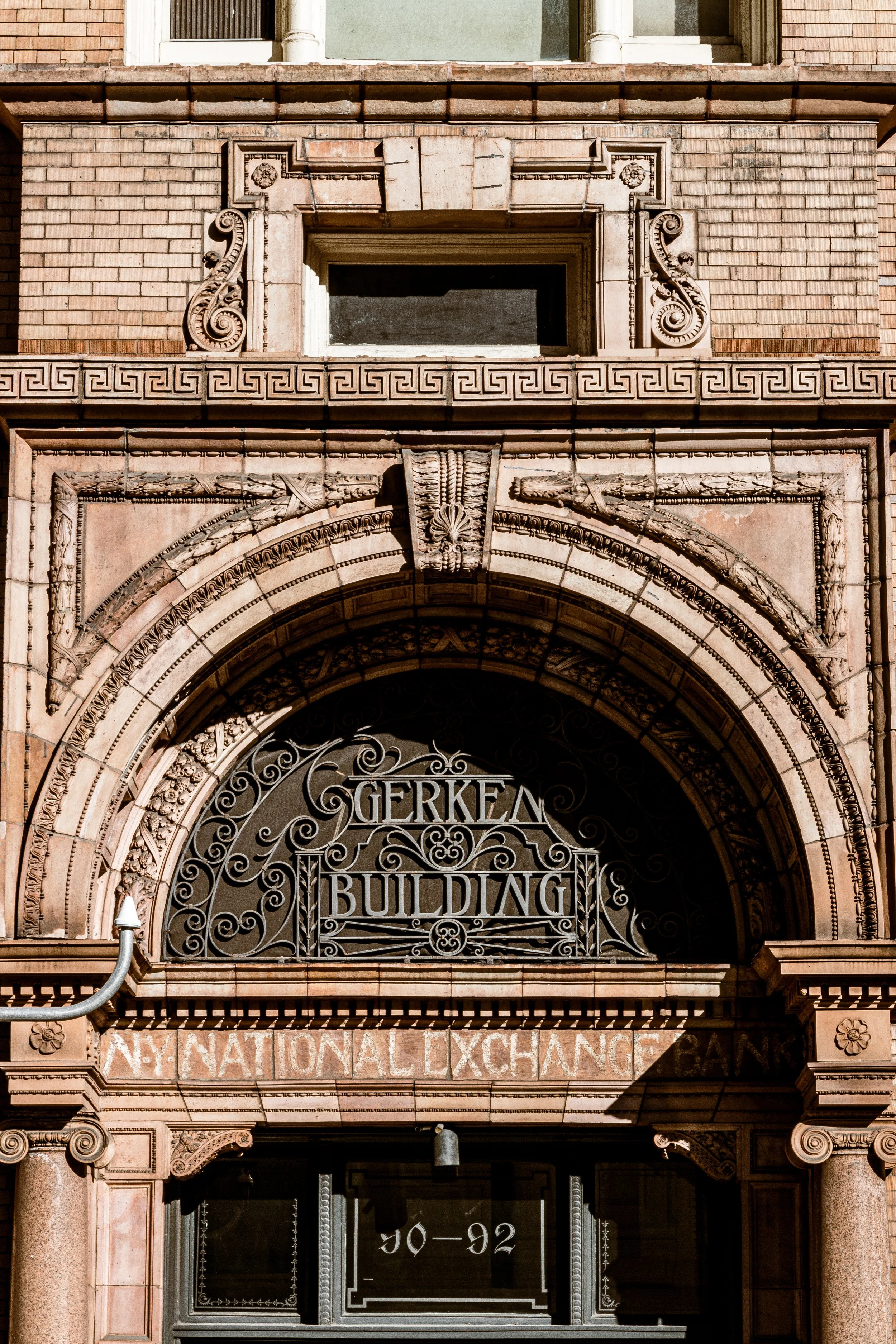 Close-up of the ornate entrance of the Gerken Building, featuring detailed stone carvings, decorative ironwork with the words 'Gerken Building,' and an old signage for 'NY National Exchange Bank.'