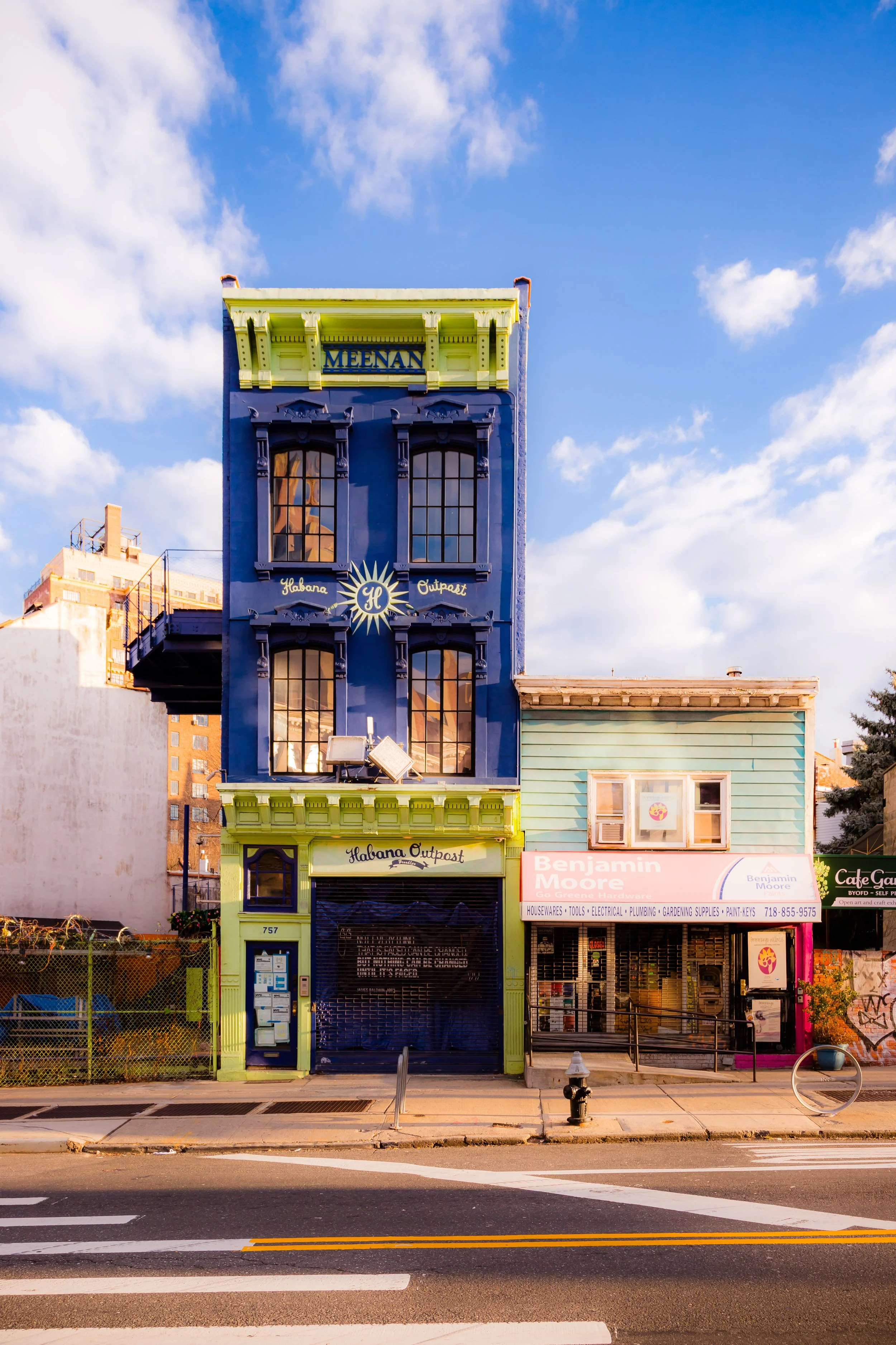 Colorful buildings with a blue and yellow facade on the left and a pastel green and pink storefront on the right, situated along a street with a crosswalk and a fire hydrant.