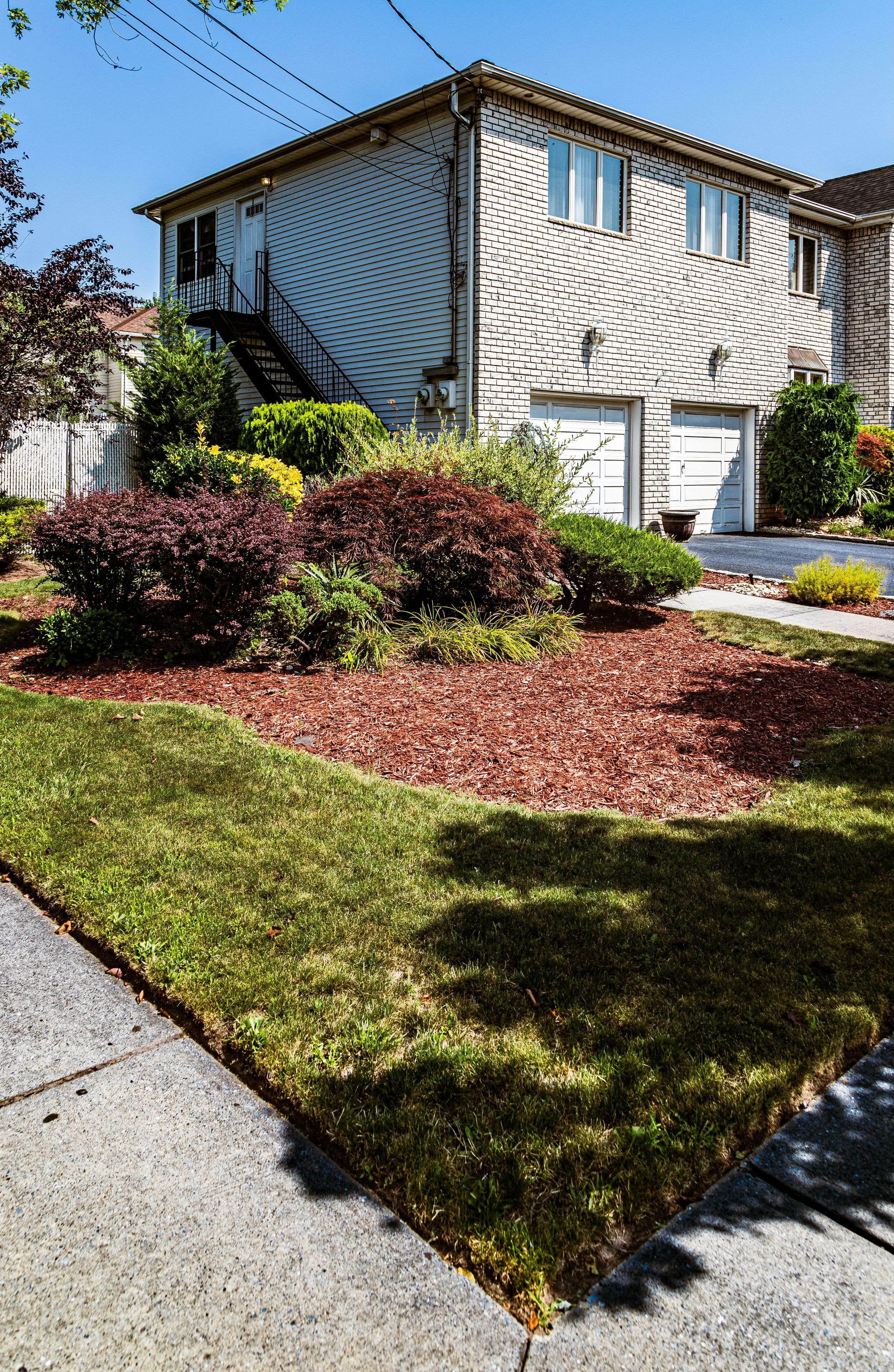 Front yard of a residential house with landscaped garden, bushes, and a sidewalk.