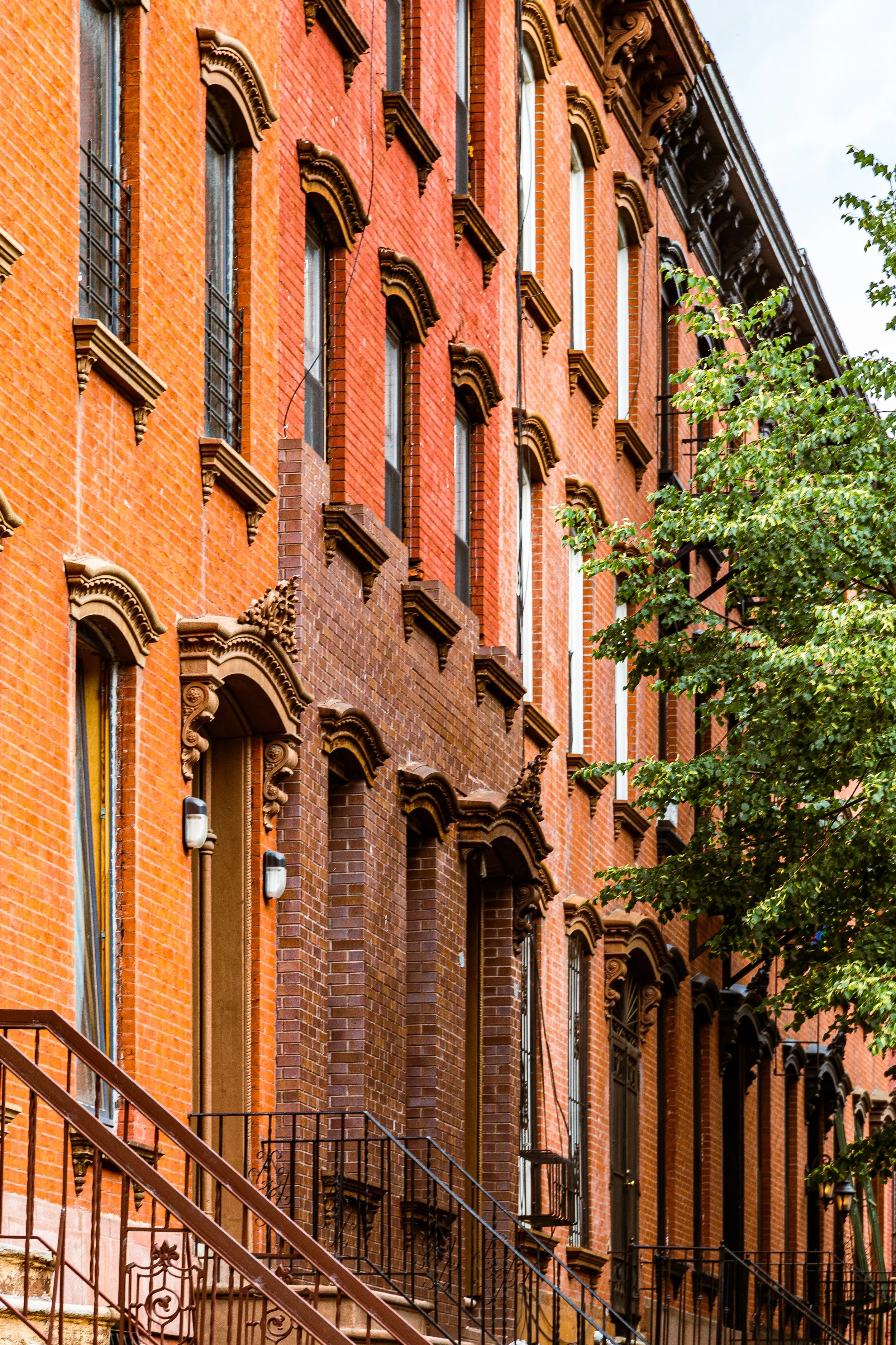 Close-up of a historic red brick building with decorative window moldings and iron fire escapes, and a tree in front.