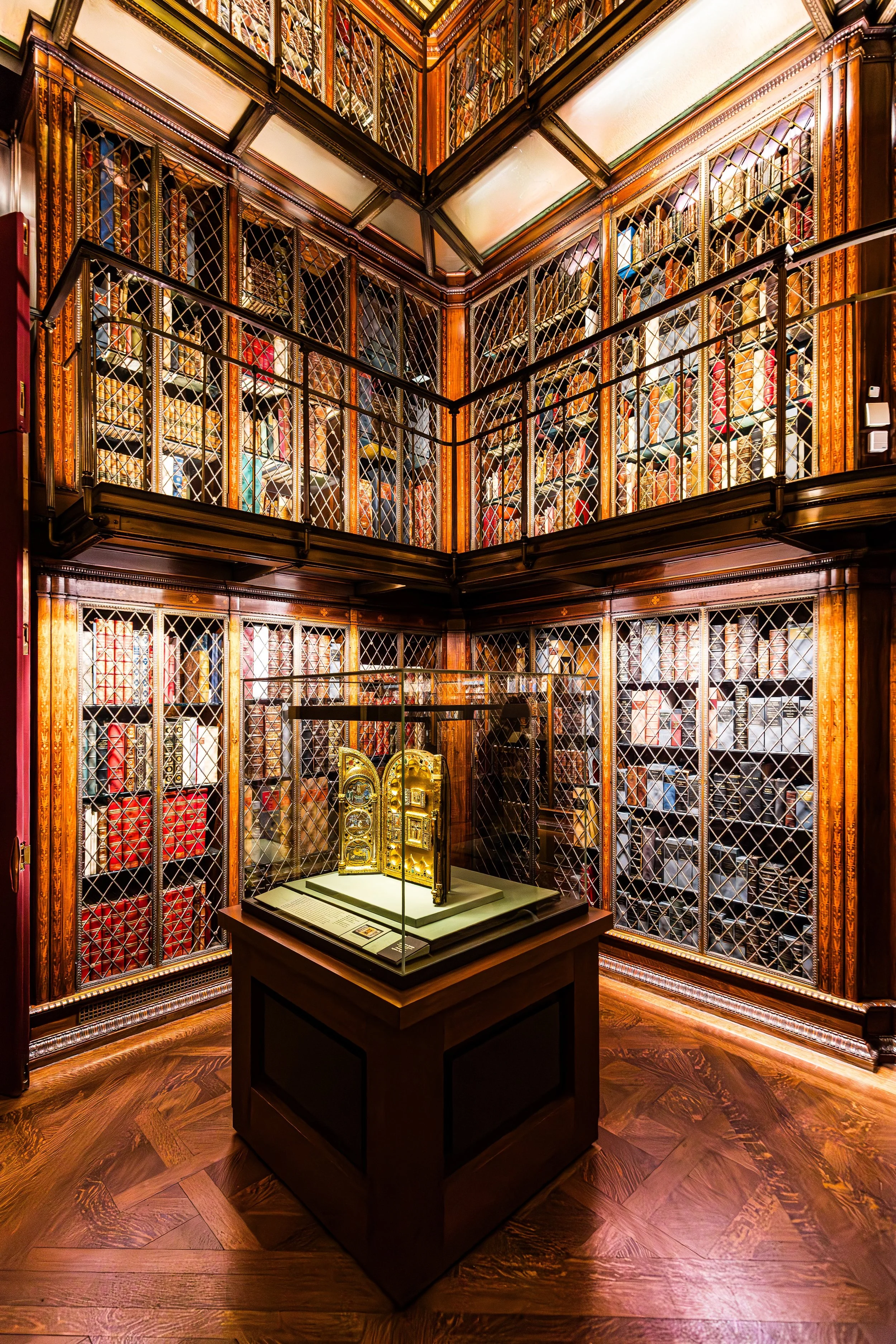 A room in a library with wooden shelves filled with books, behind glass windows with diamond-shaped lattice patterns, a display case with an ornate golden clock.