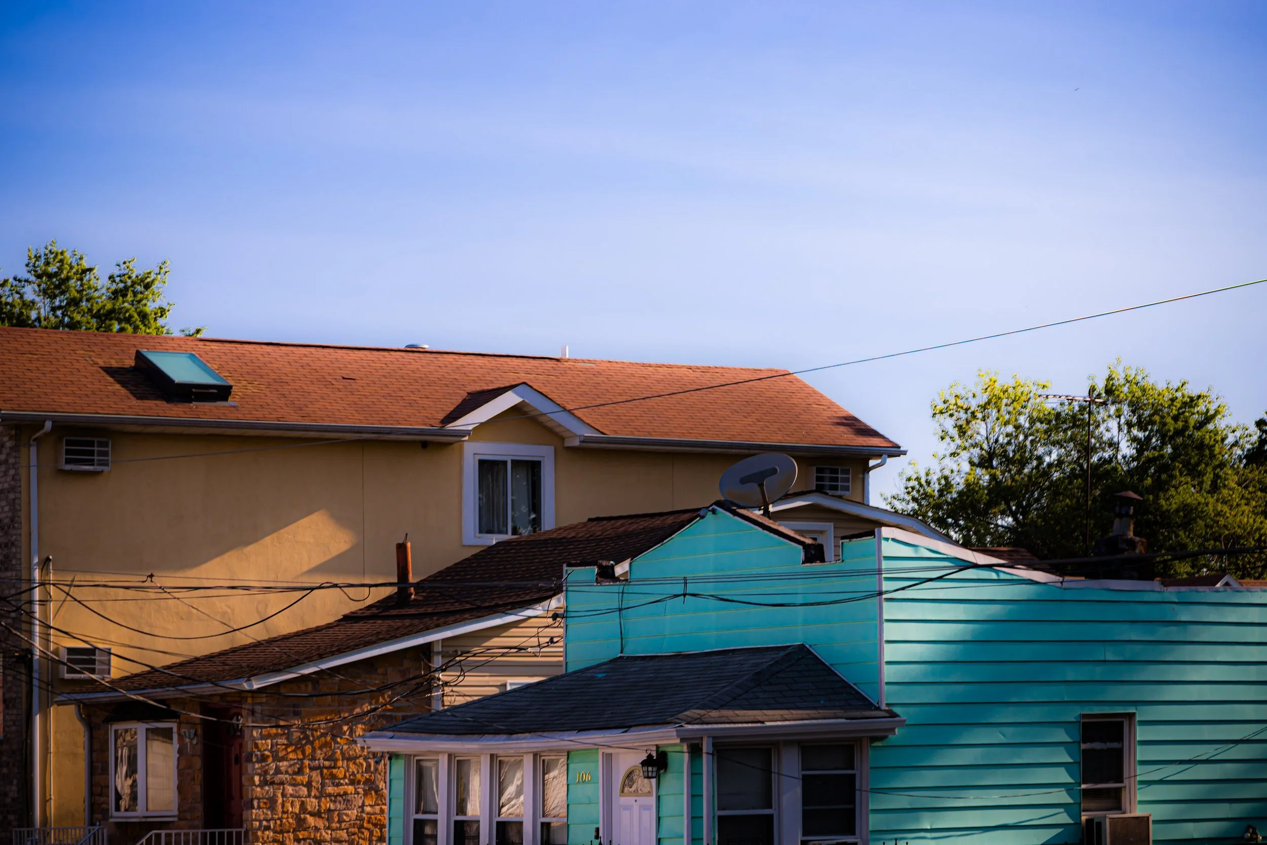 Multiple houses with different colored exteriors and rooftops, trees, and a clear blue sky in the background.