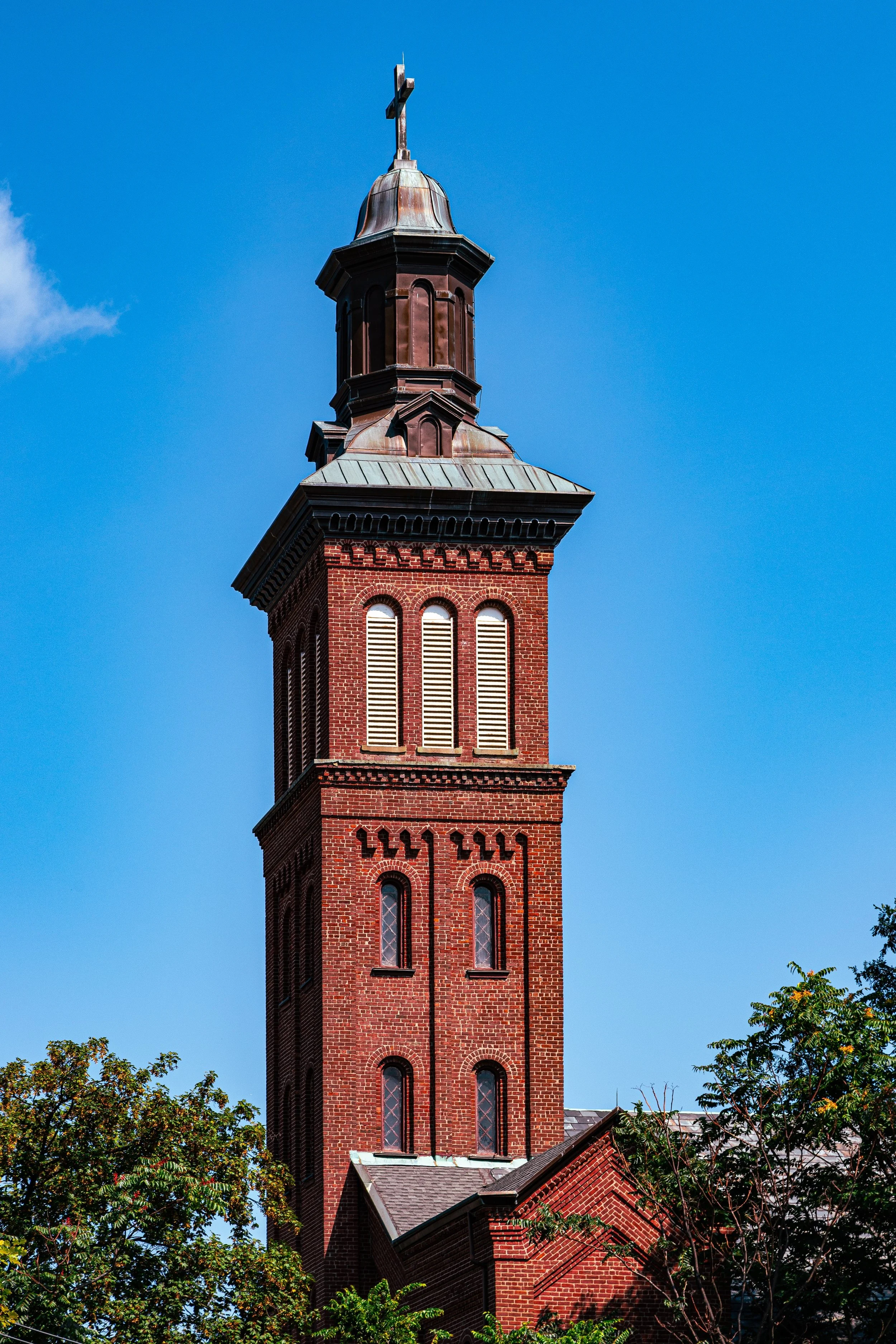 A tall brick church steeple with a cross at the top, set against a bright blue sky.