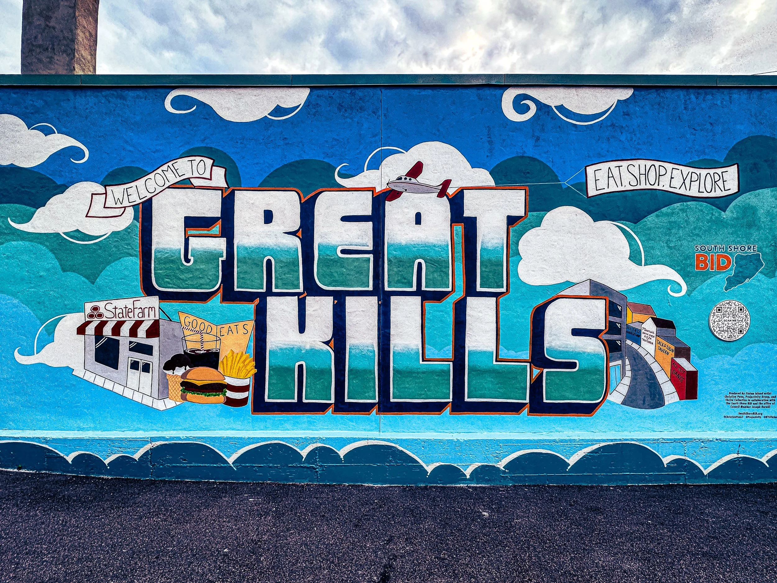 Colorful mural featuring the words 'Great Keys' with illustrations of clouds, a boat, a building labeled 'State Farm,' food items like a burger and fries, a plane, a mountain, a QR code, and various signs with phrases such as 'Welcome to,' 'Eat, Shop, Explore,' and 'South Shore BID.'