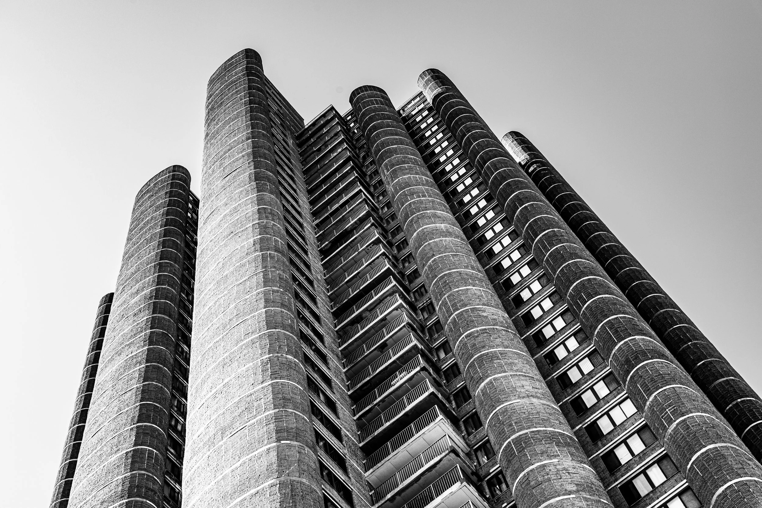 Low-angle view of a tall, modern skyscraper with cylindrical towers against a clear sky.
