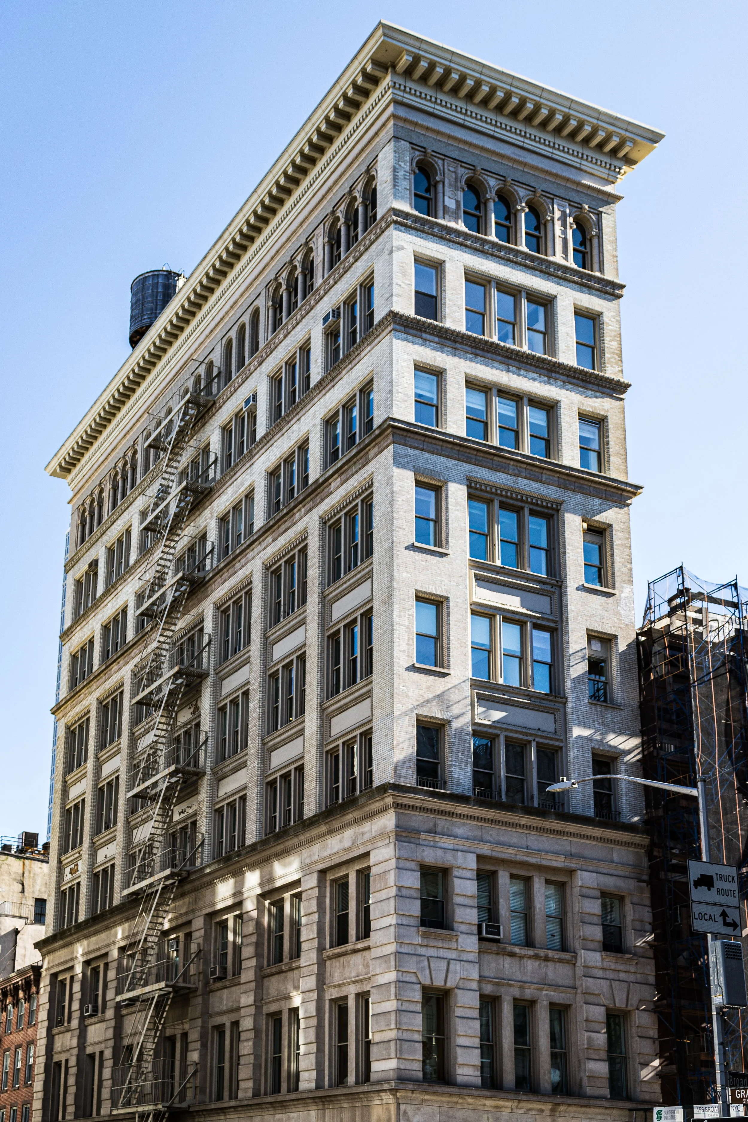 A tall, beige, multi-story building with large windows and decorative architectural details, situated in an urban area under a clear blue sky.
