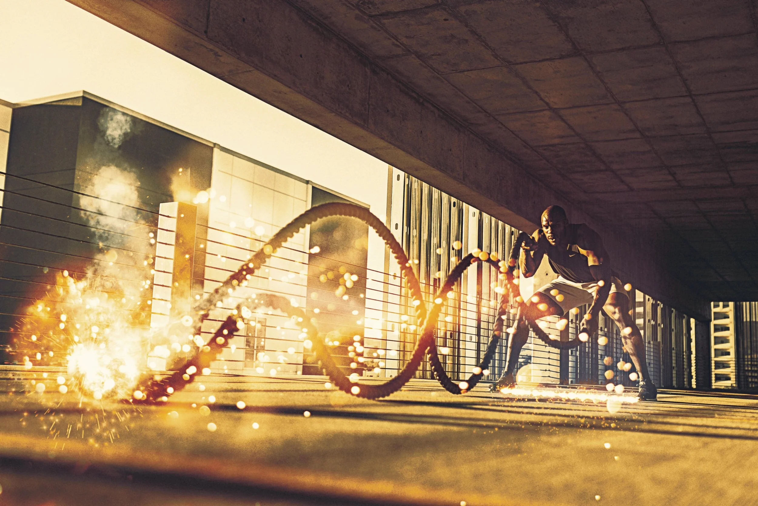 Ein Mann in Sportkleidung trainiert auf einer urbanen Dachterrasse bei Sonnenuntergang, während Funken und Rauch um ihn herum fliegen.