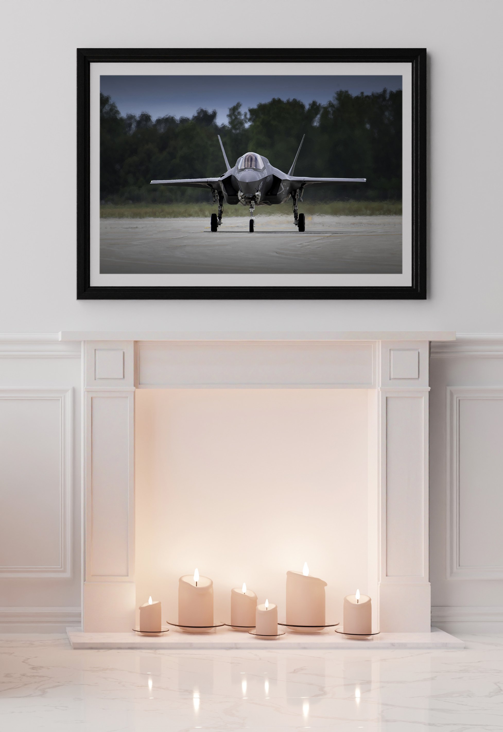 A framed picture of a fighter jet on a runway hanging above a white fireplace with six lit candles on the hearth.