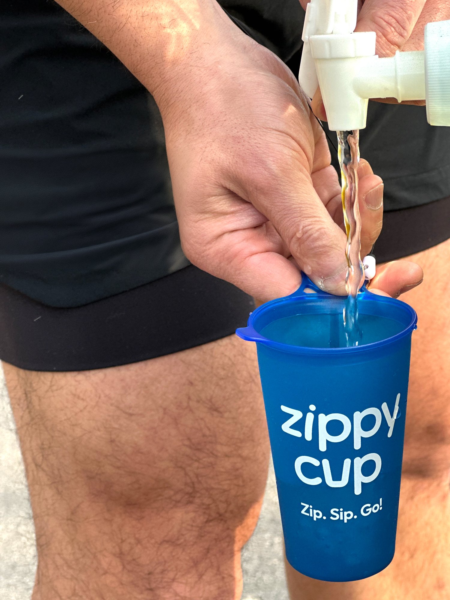A person filling a blue Zippy Cup with water from a faucet.