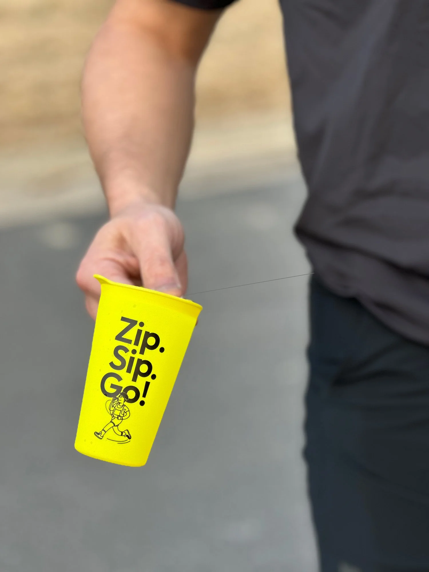 A person holding a bright yellow Zippy Cup with the text 'Zip. Sip. Go!.!