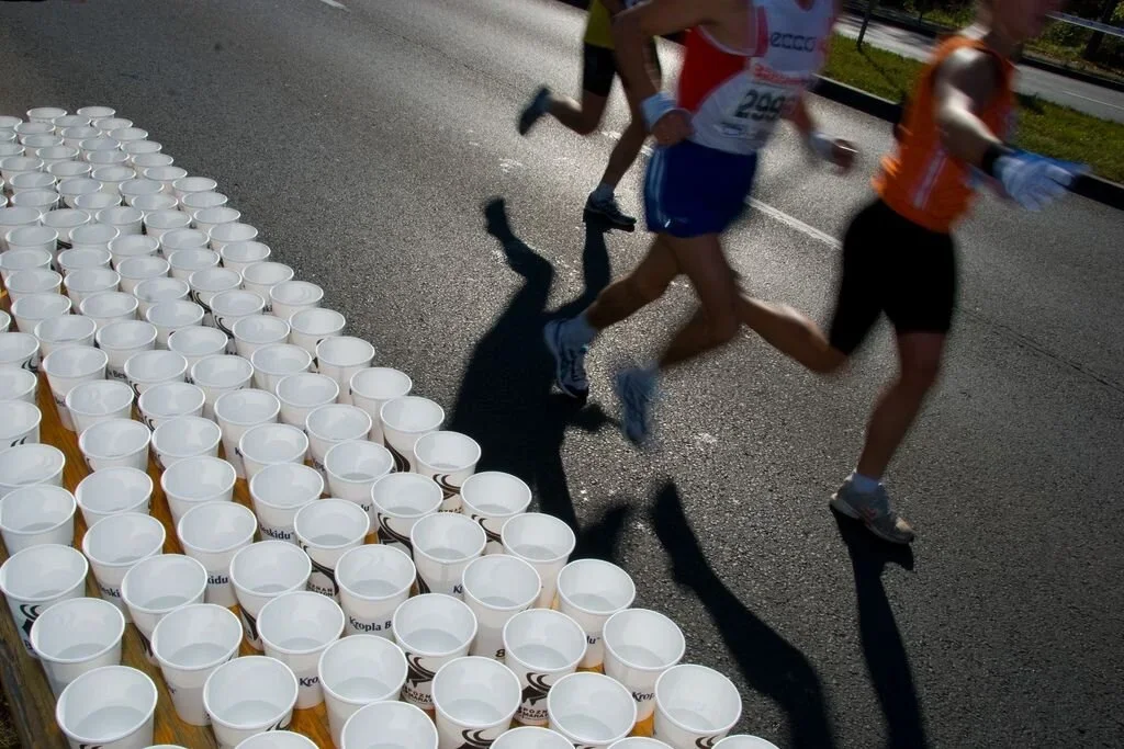 Marathon runners crossing the finish line next to a table of empty paper cups.