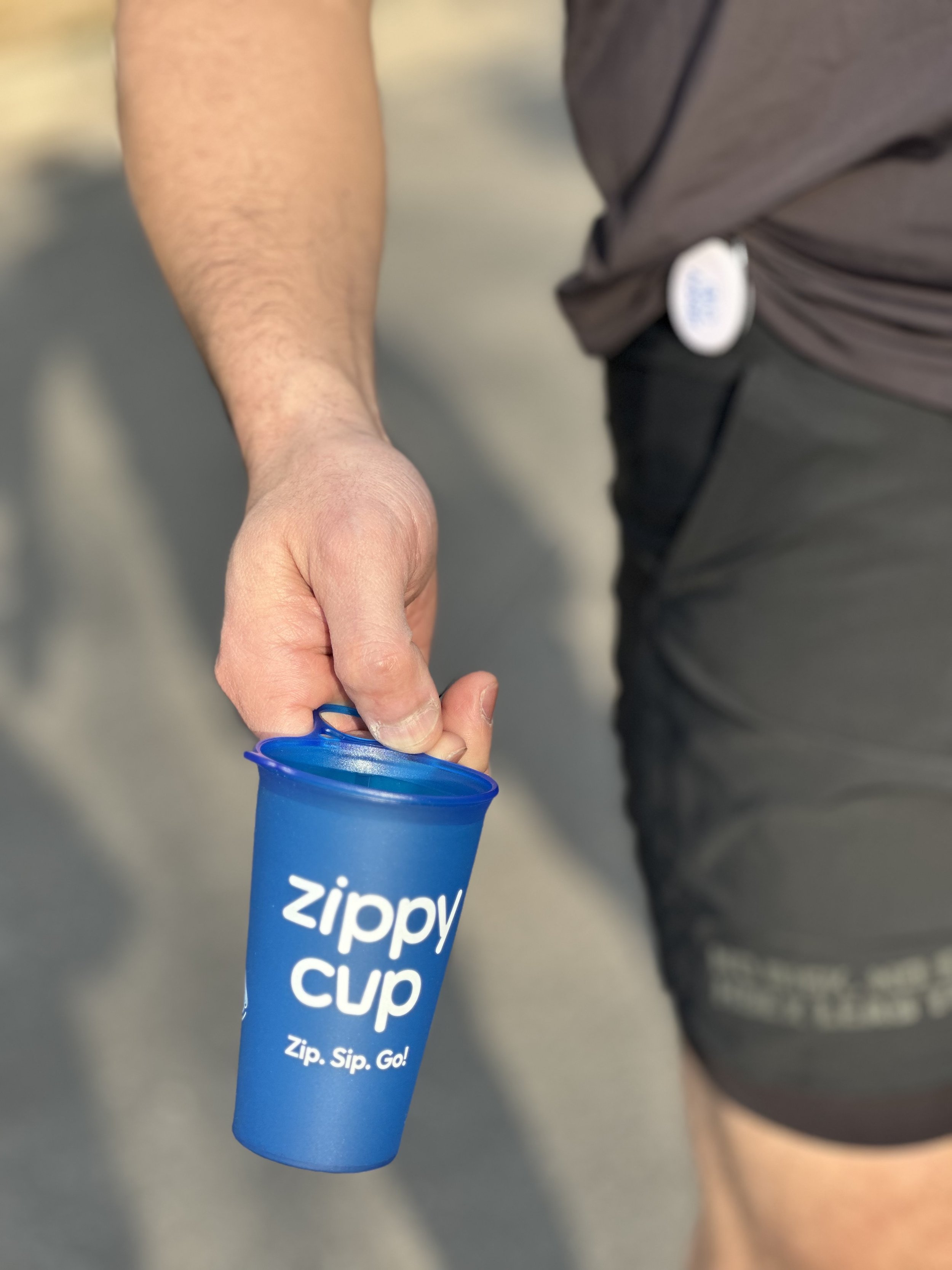 A person holding a blue Zippy Cup with the logo and the slogan "Zip. Sip. Go!" written on it.