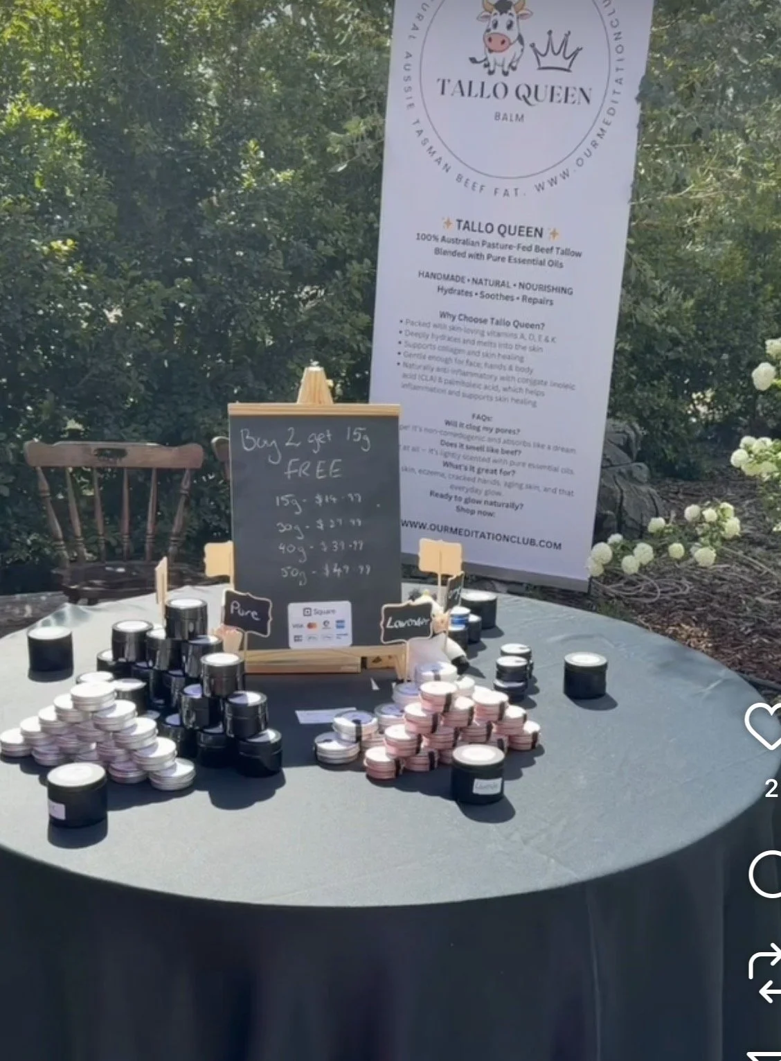 A table with small jars of balm, a sign with prices, and larger sign/banner behind advertising Tallo Queen beef balm.