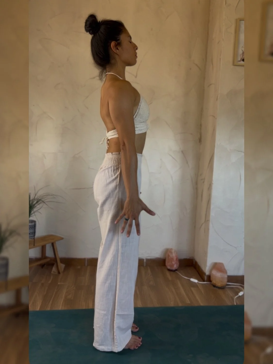 Mujer realizando ejercicio de postura de yoga en interiores con pared de fondo y suelo de madera.