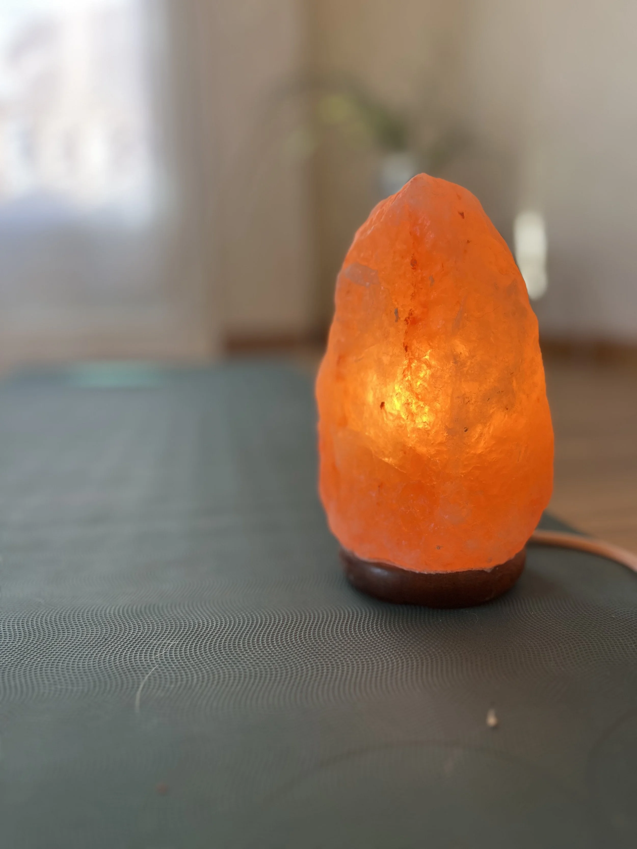 Lámpara en forma de roca de sal del Himalaya, con luz encendida dentro, sobre una mesa