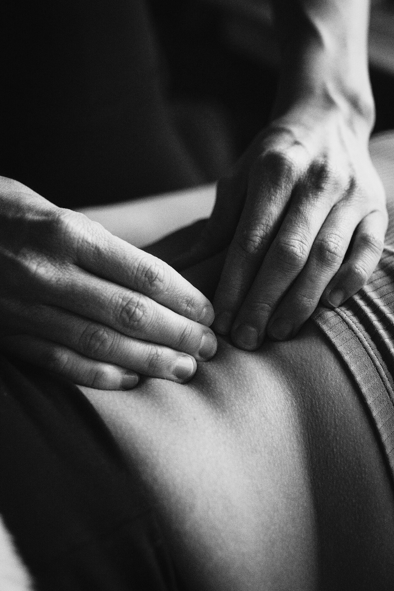 Nahaufnahme von Händen, die auf einen Oberschenkel drücken, in schwarz-weiß.