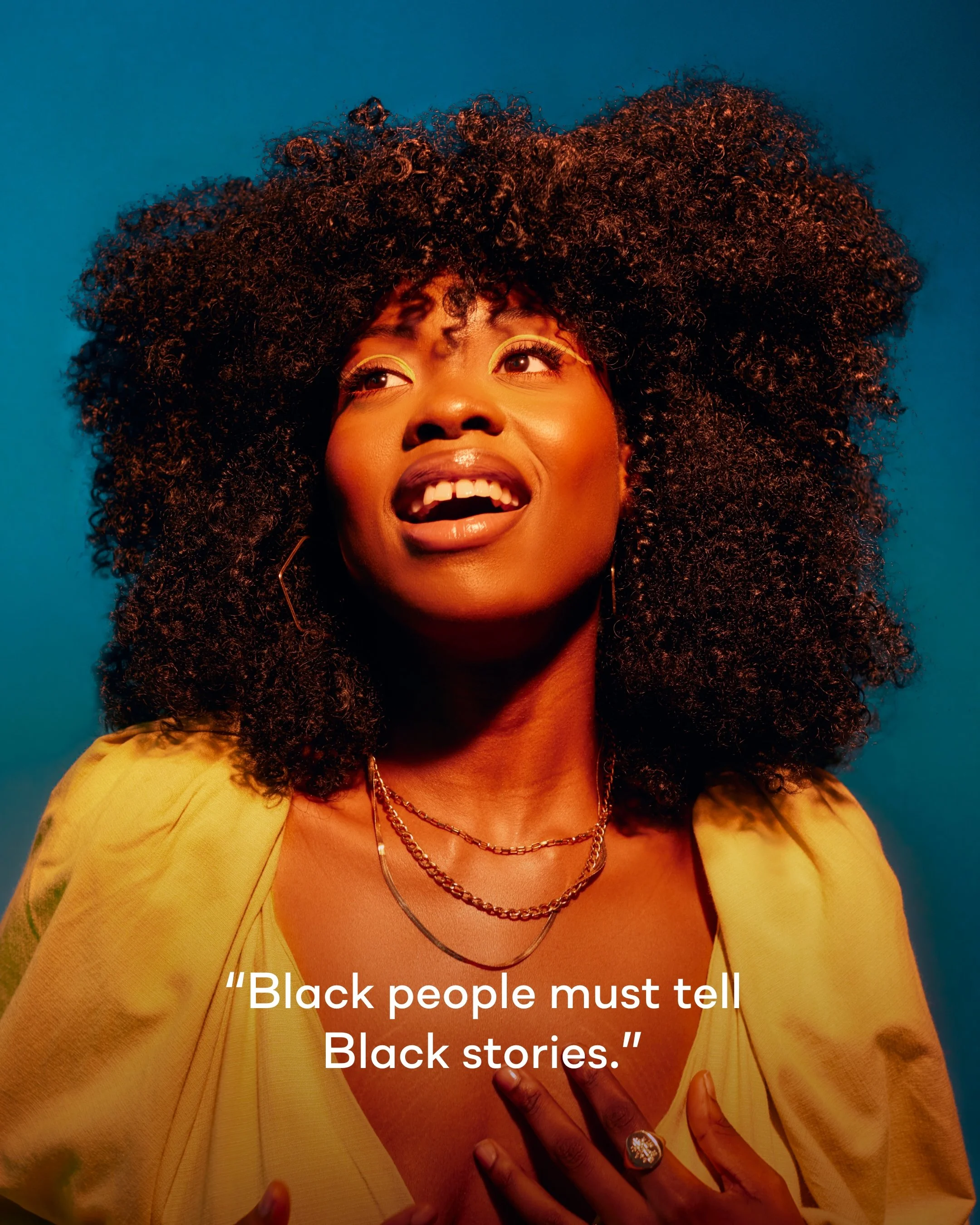 A woman with curly hair and multiple necklaces, wearing a yellow blazer, speaking poetic words about Black stories and Black people, as seen in the partially visible quote, 'Black people must tell Black stories.'