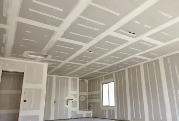 Empty room with drywall installed on walls and ceiling, showing unfinished construction inside a building.