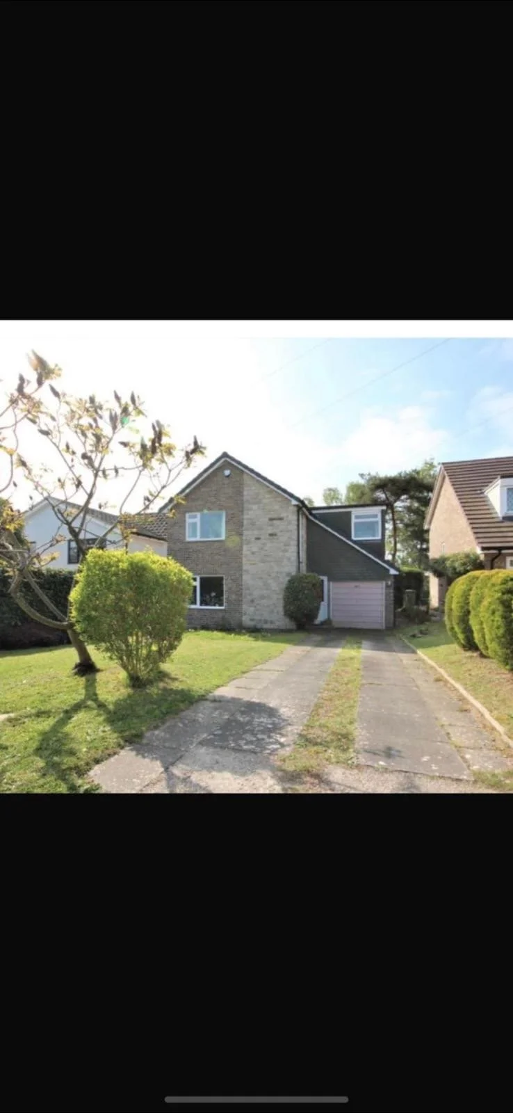 A suburban house with a driveway, surrounded by a lawn and shrubs, under a partly cloudy sky.