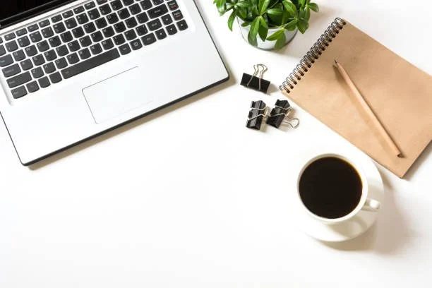 Espace de travail avec un ordinateur portable, une plante, un bloc-notes, un crayon, des trombones, des pinces à cheveux et une tasse de café.