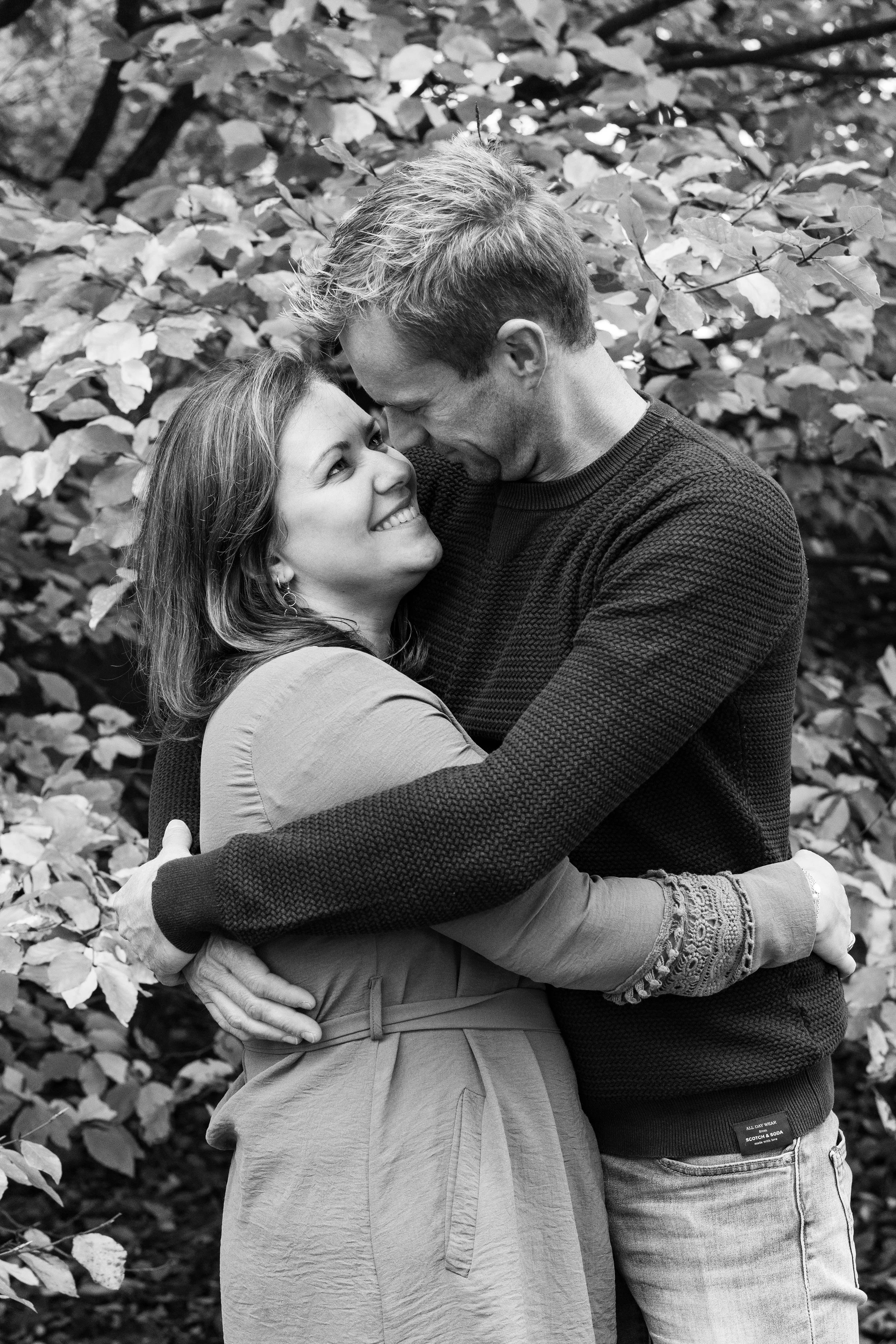 Un couple souriant et s'embrassant dans un parc avec des arbres en arrière-plan.