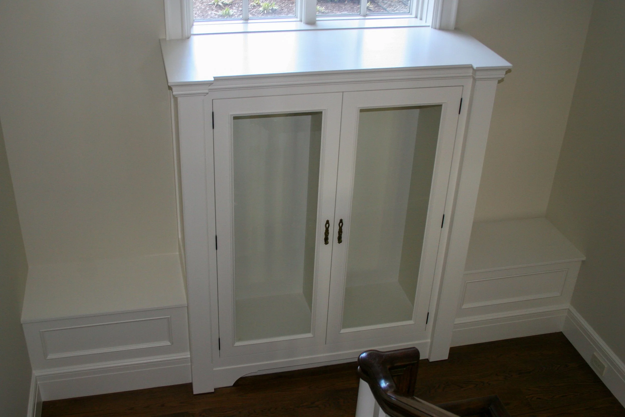 Custom white cabinet with glass doors in stair landing and benches on either side 
