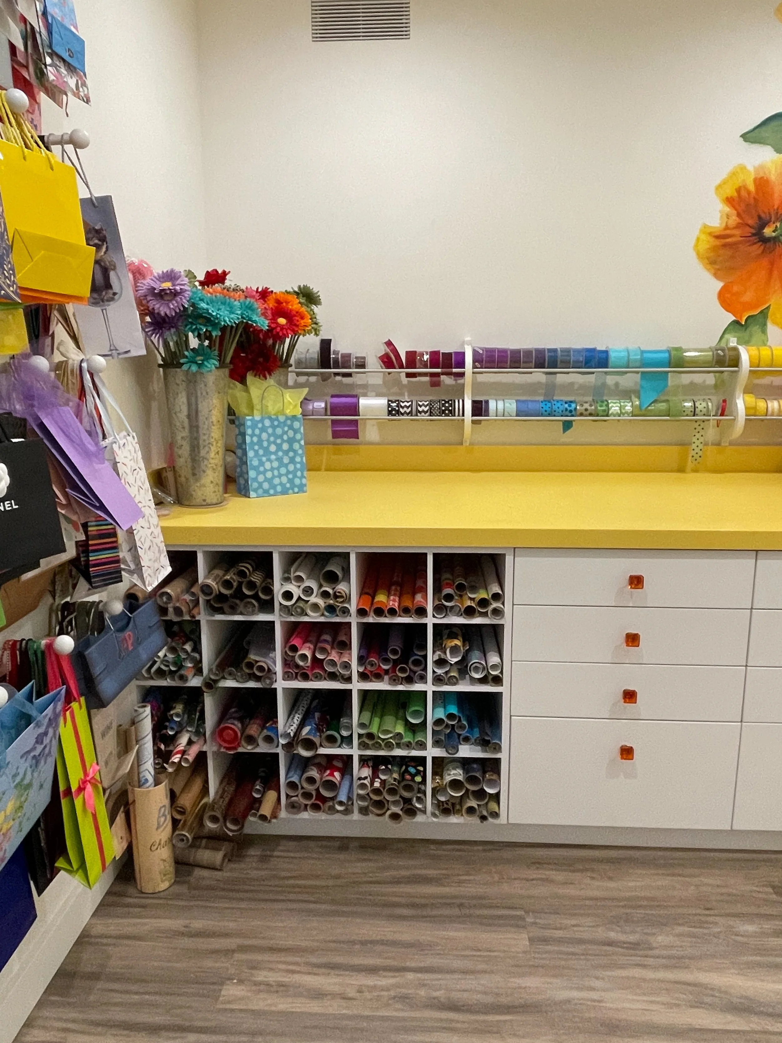 White craft room with yellow countertops, floral wallpaper and custom ribbon and wrapping paper storage 