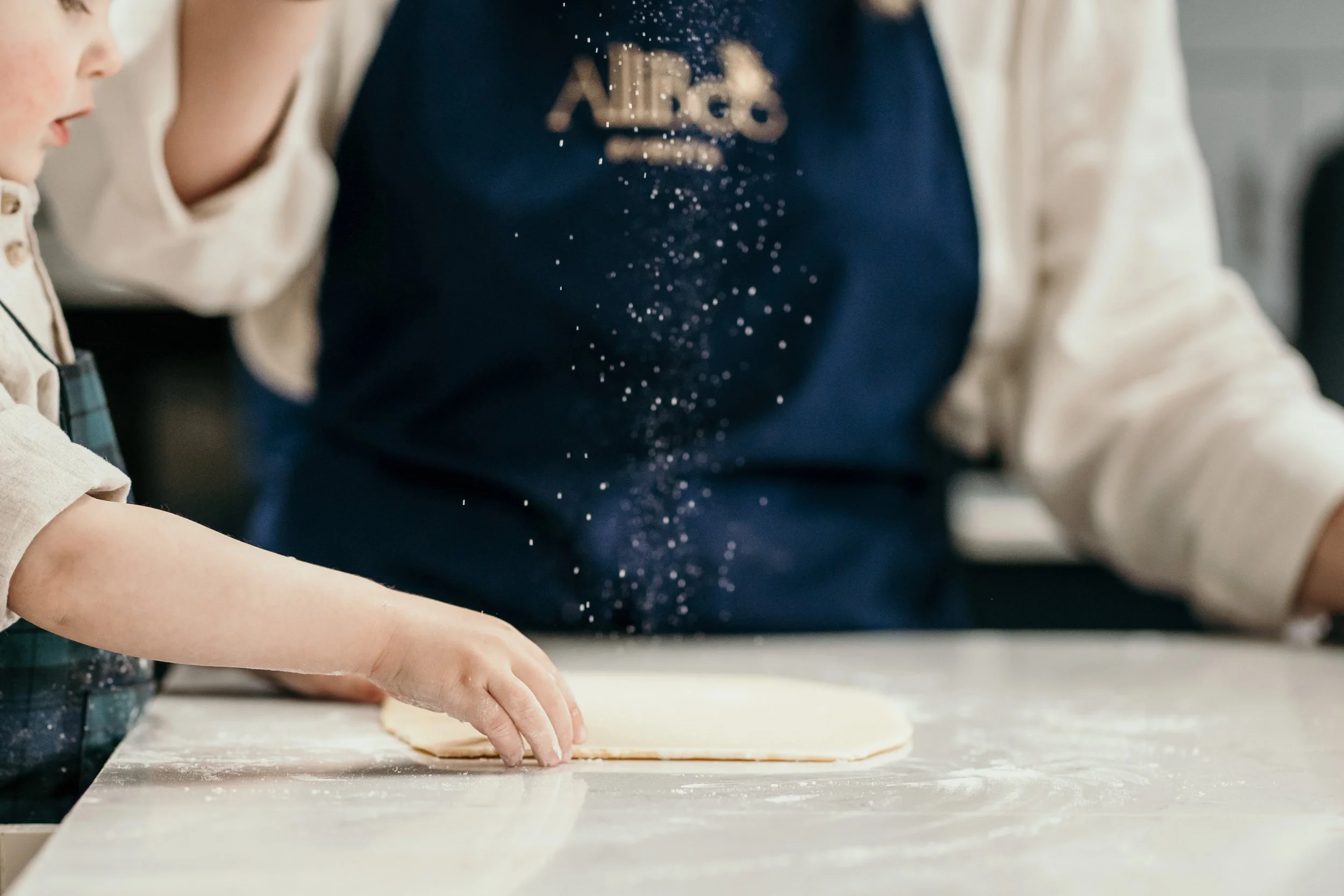 Child rolling cookie dough in an apron.