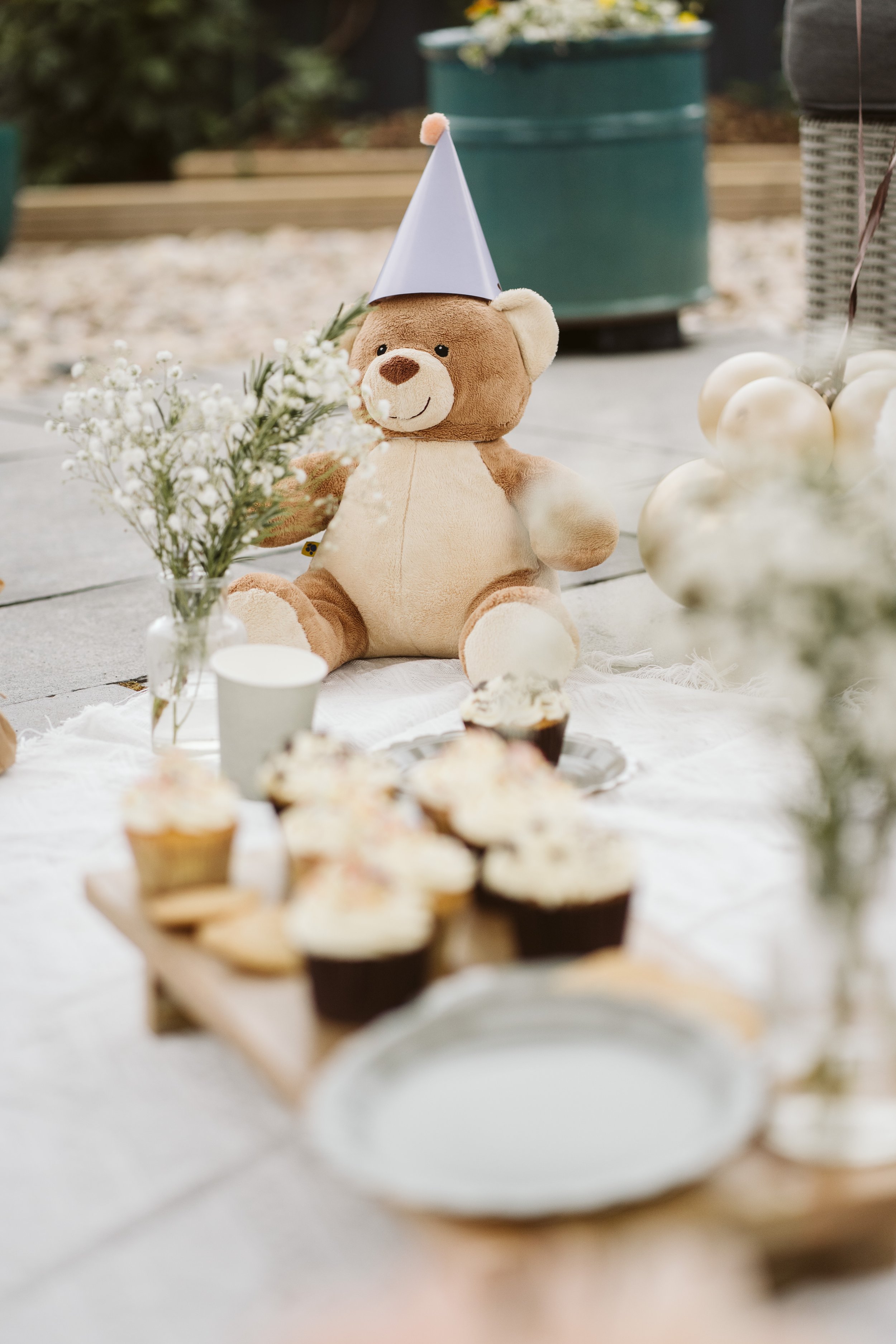 Teddy bear-themed afternoon tea with cakes and flowers.