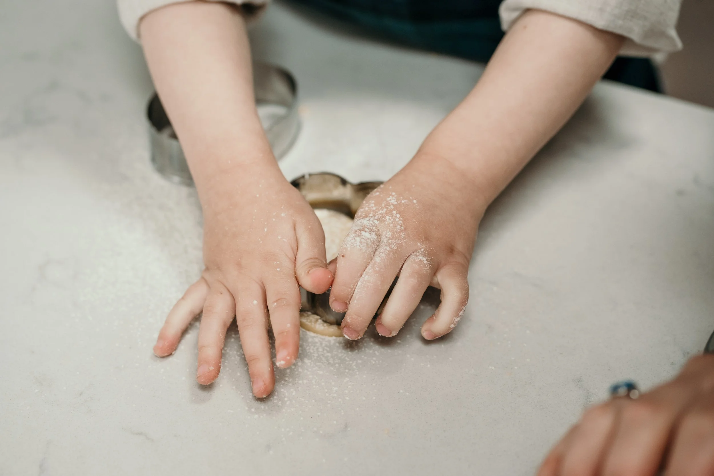 Small hands rolling cookie dough on a floured surface.