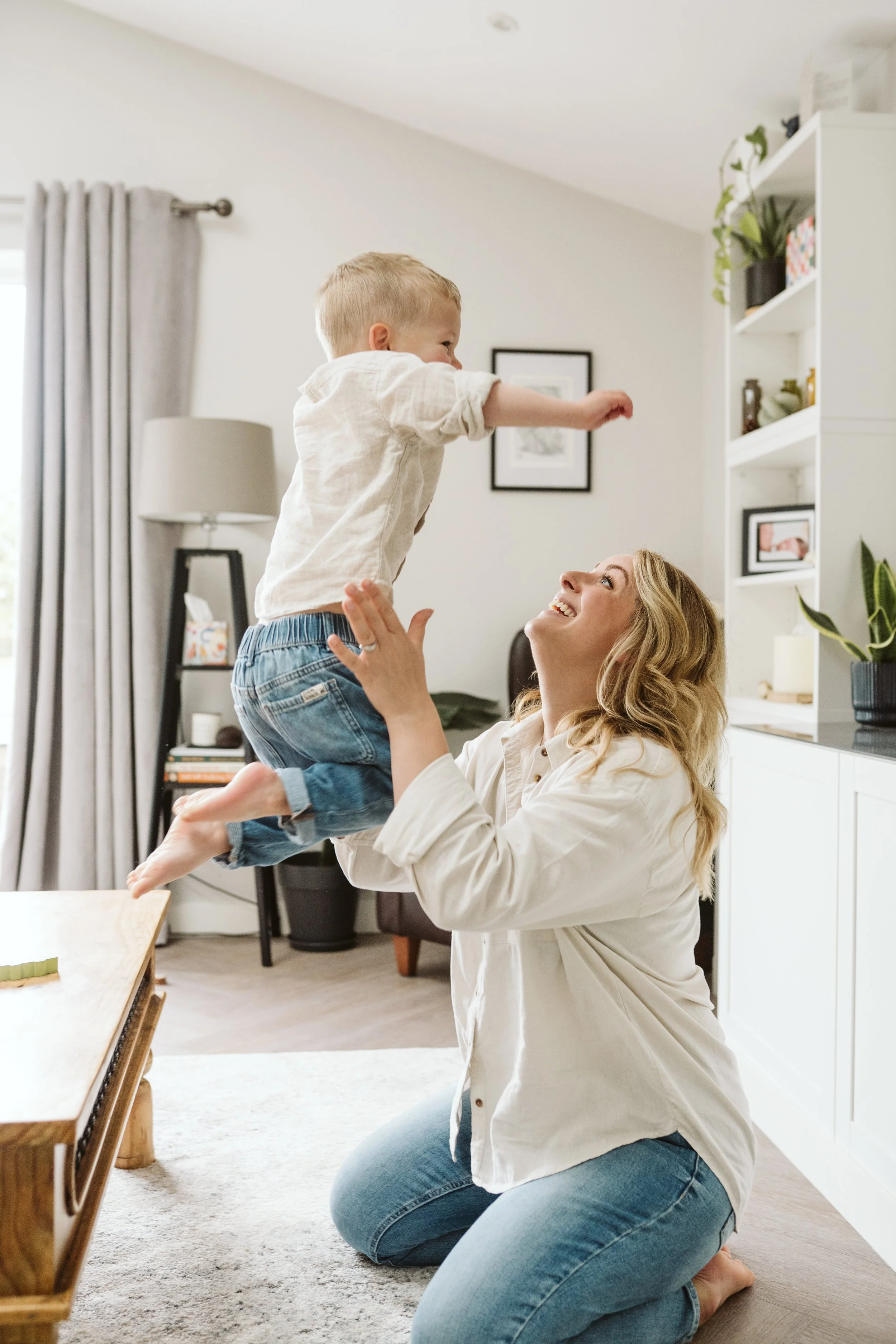 Child jumping off table into mums arms in living room. 