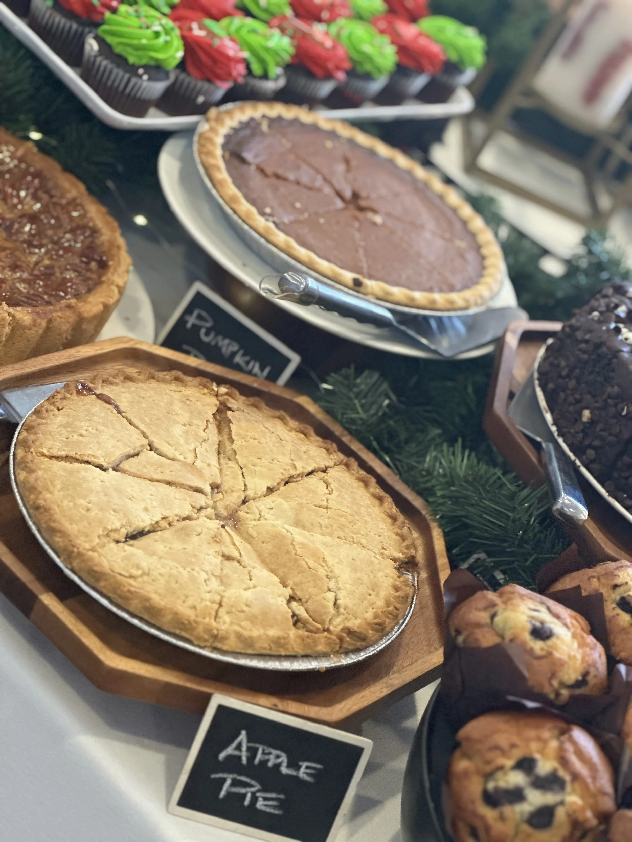 Assorted baked desserts including apple pie, pumpkin pie, and muffins on a display table.
