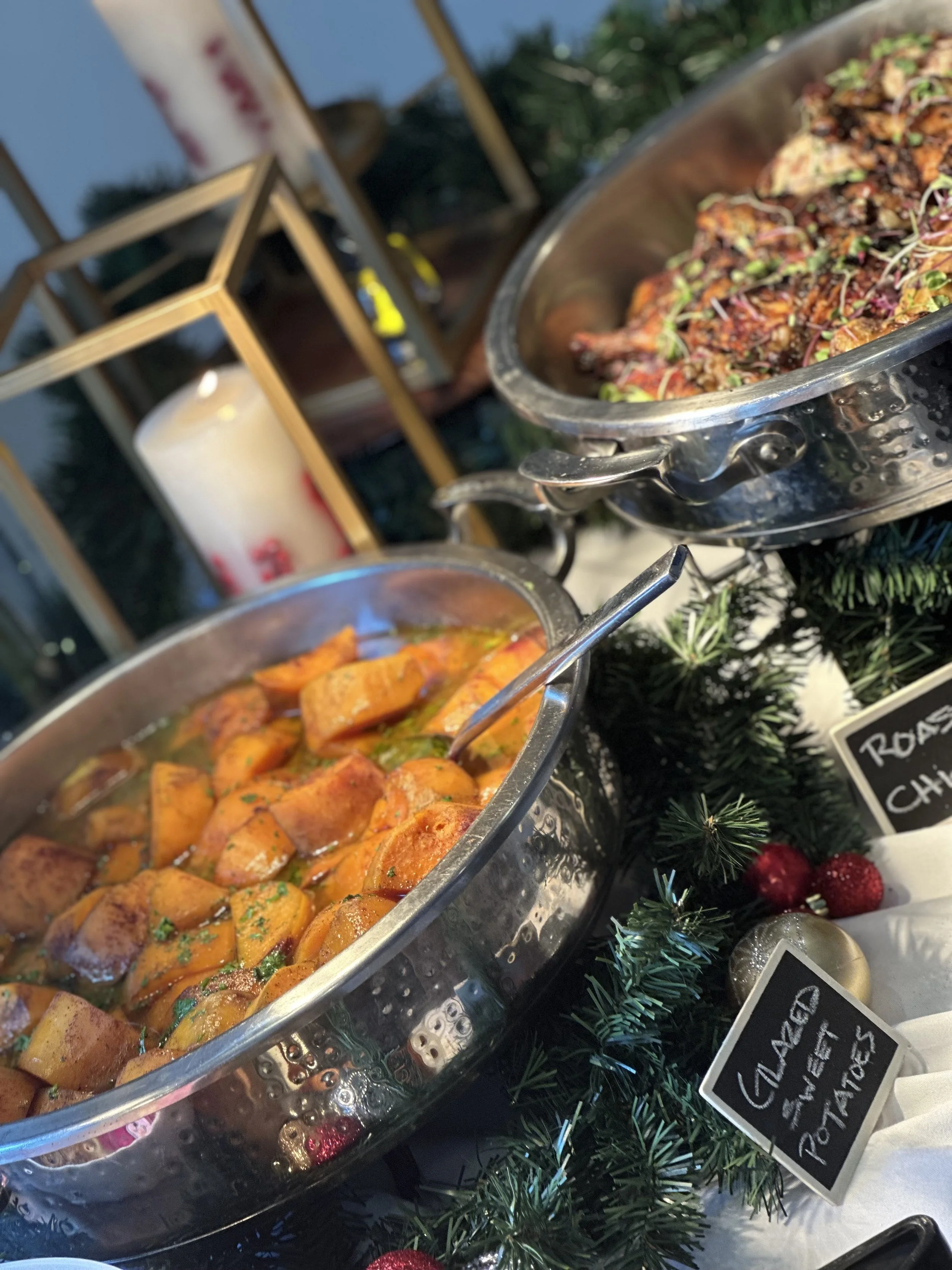Holiday buffet with roasted sweet potatoes and roasted chicken with herbs surrounded by Christmas decorations.