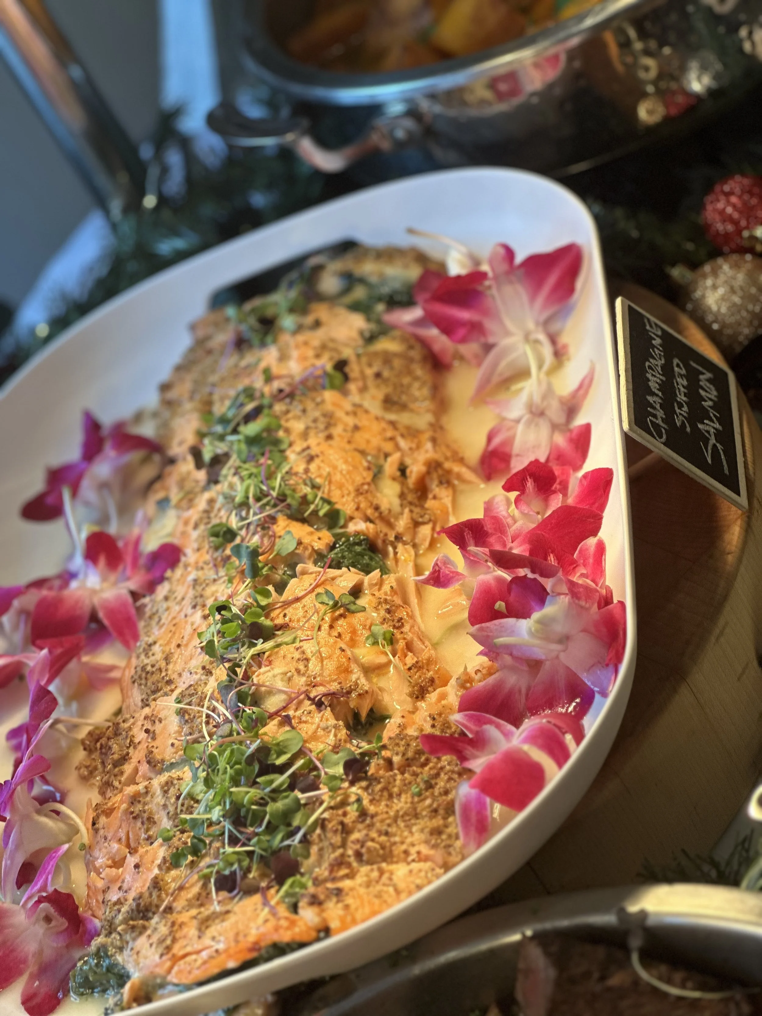 Salmon fillet garnished with microgreens and surrounded by pink and white flower petals in a white oval dish.
