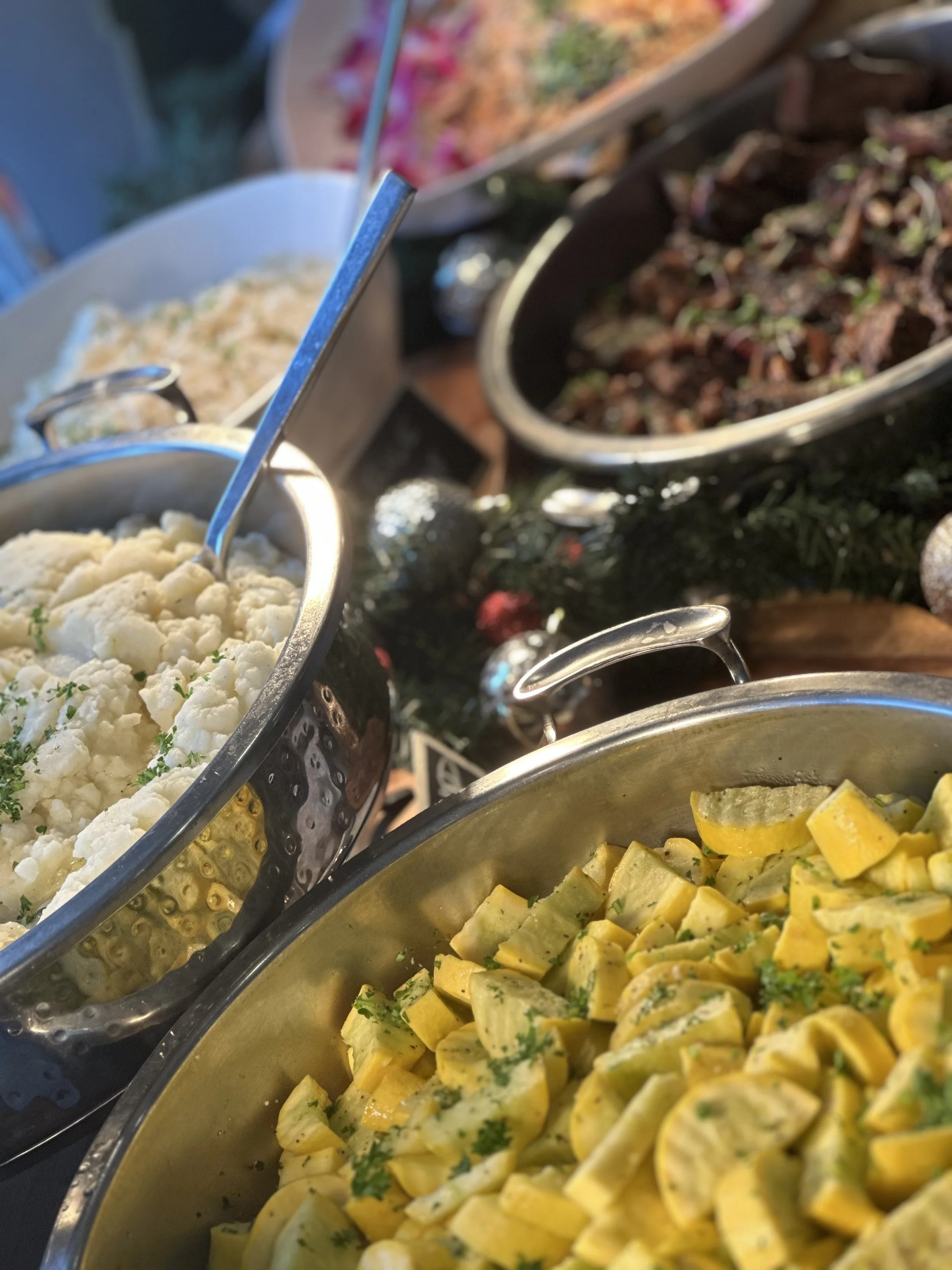 Close-up of a buffet table with bowls of mashed potatoes, chopped squaw, and shredded meat, decorated with holiday ornaments.