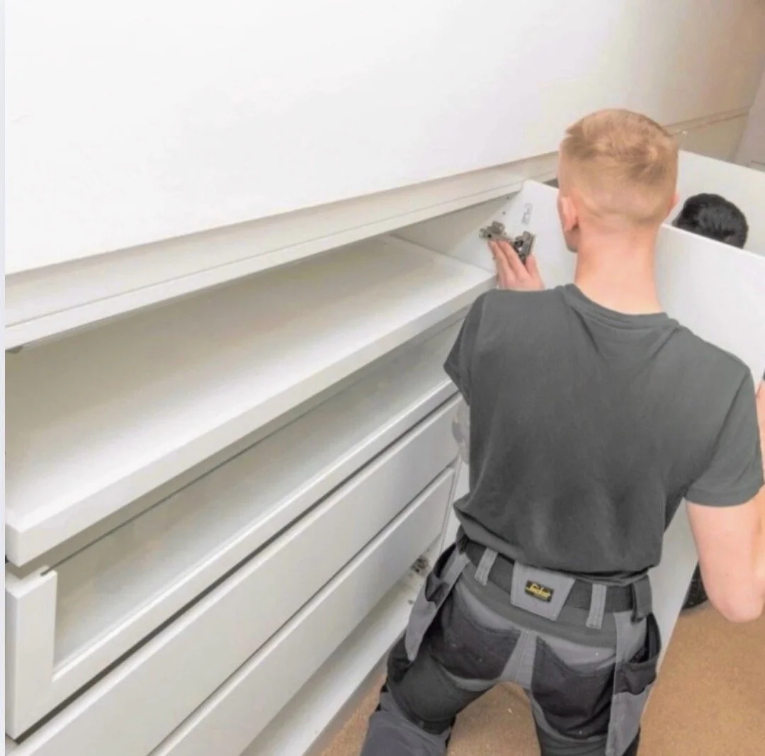 A man with blond hair in work clothes installing a bespoke wardrobe.