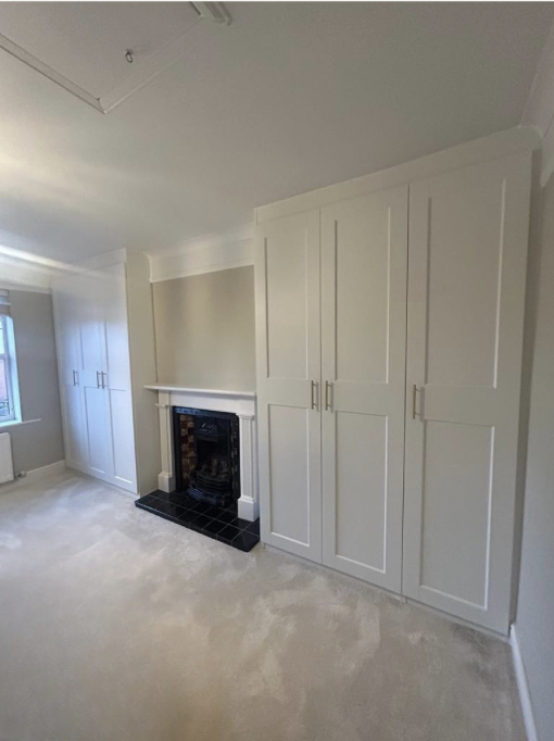 Empty room with built-in white cabinets, a black fireplace, a window, and beige carpet.