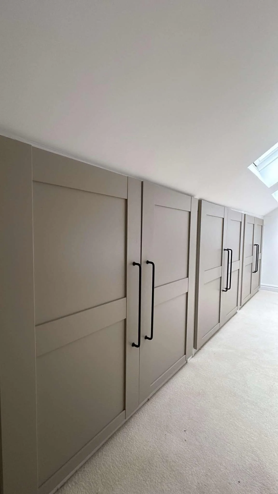 Light gray cabinets with black handles in an attic with a sloped ceiling and a skylight window.