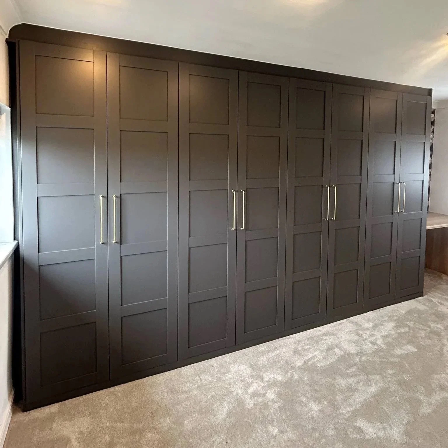 A large dark wood cabinet with multiple paneled doors and gold handles, situated on a beige carpeted floor in a room.