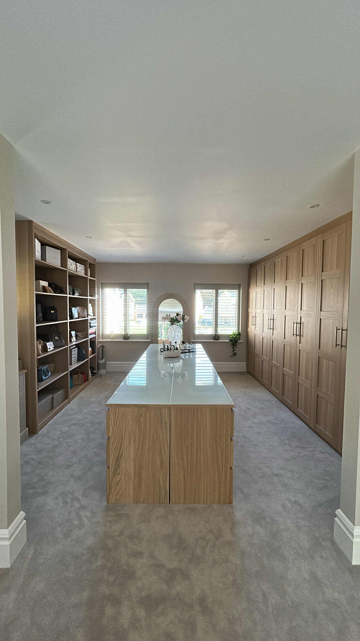 Bright dining room with wooden cabinetry, a central table with a white surface, and windows with blinds on the far wall.