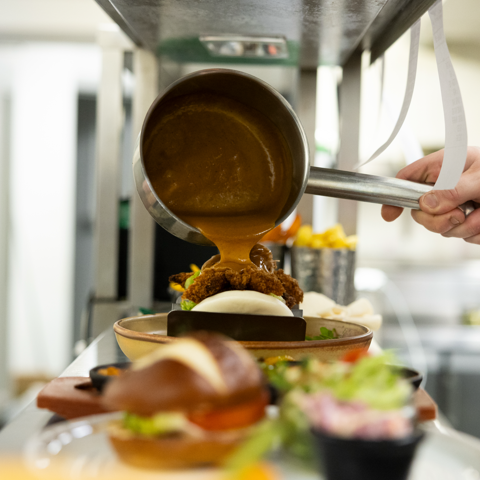 Side view of a chef plating up a dish. Shelves with bowls and plates are visible in the background.