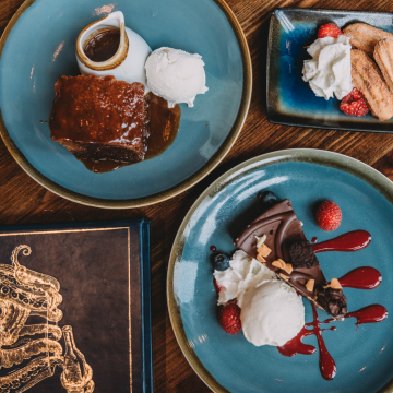 Dessert plates with chocolate cake, ice cream, whipped cream, berries, and chocolate sauce on a wooden table.