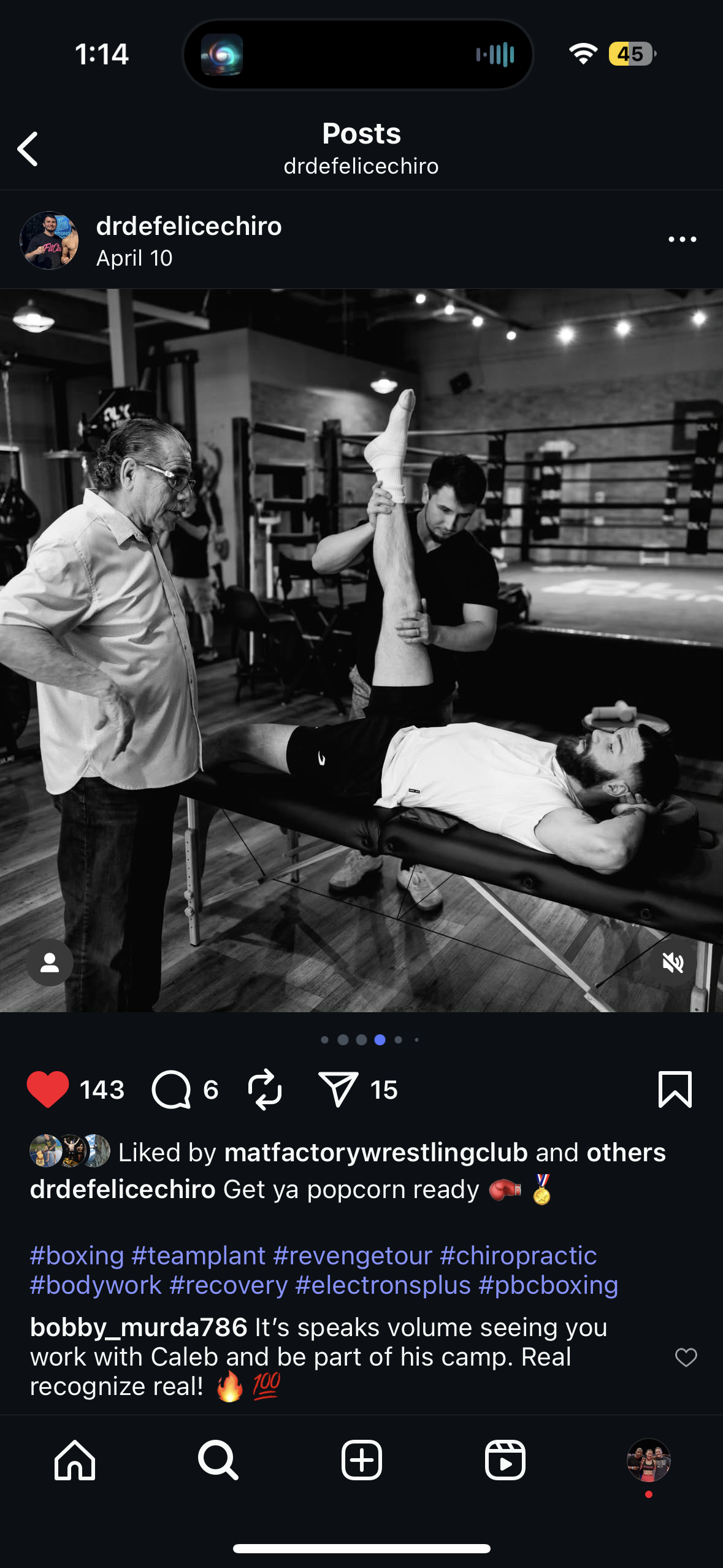 A man lying on a massage table receiving a leg stretch from a trainer, with an older man observing, in a gym or boxing training facility.