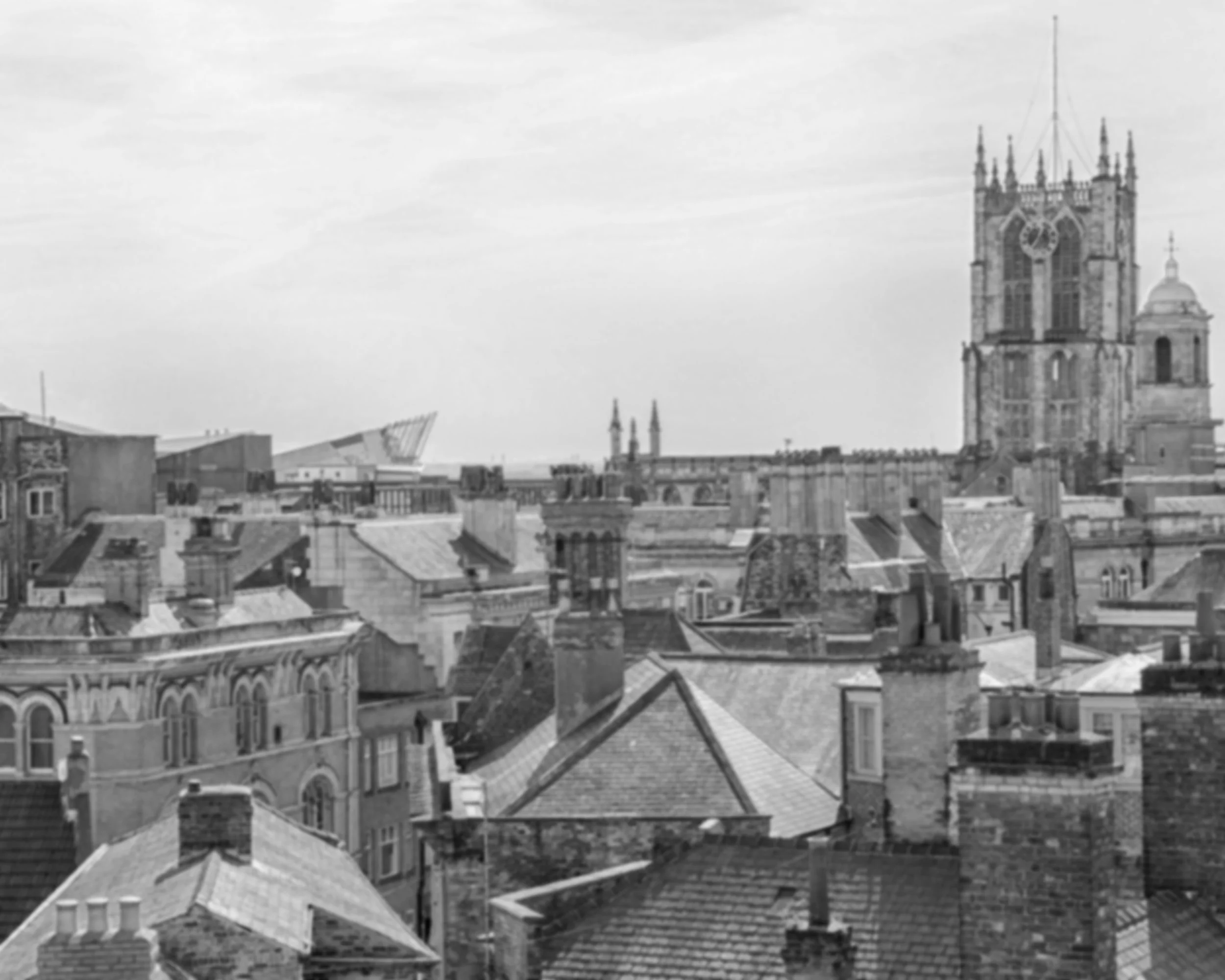 Black and white photo of a cityscape featuring historic buildings and rooftops, with a large church tower in the background.