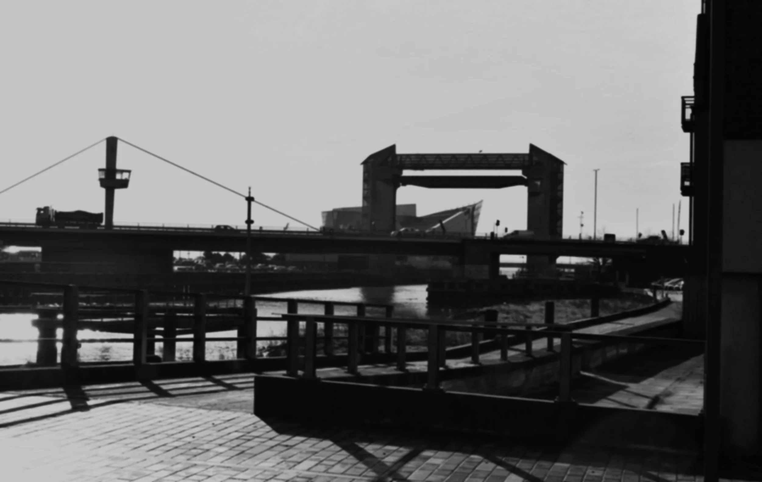 Black and white photo of a cityscape with a bridge crossing a river and modern buildings in the background.
